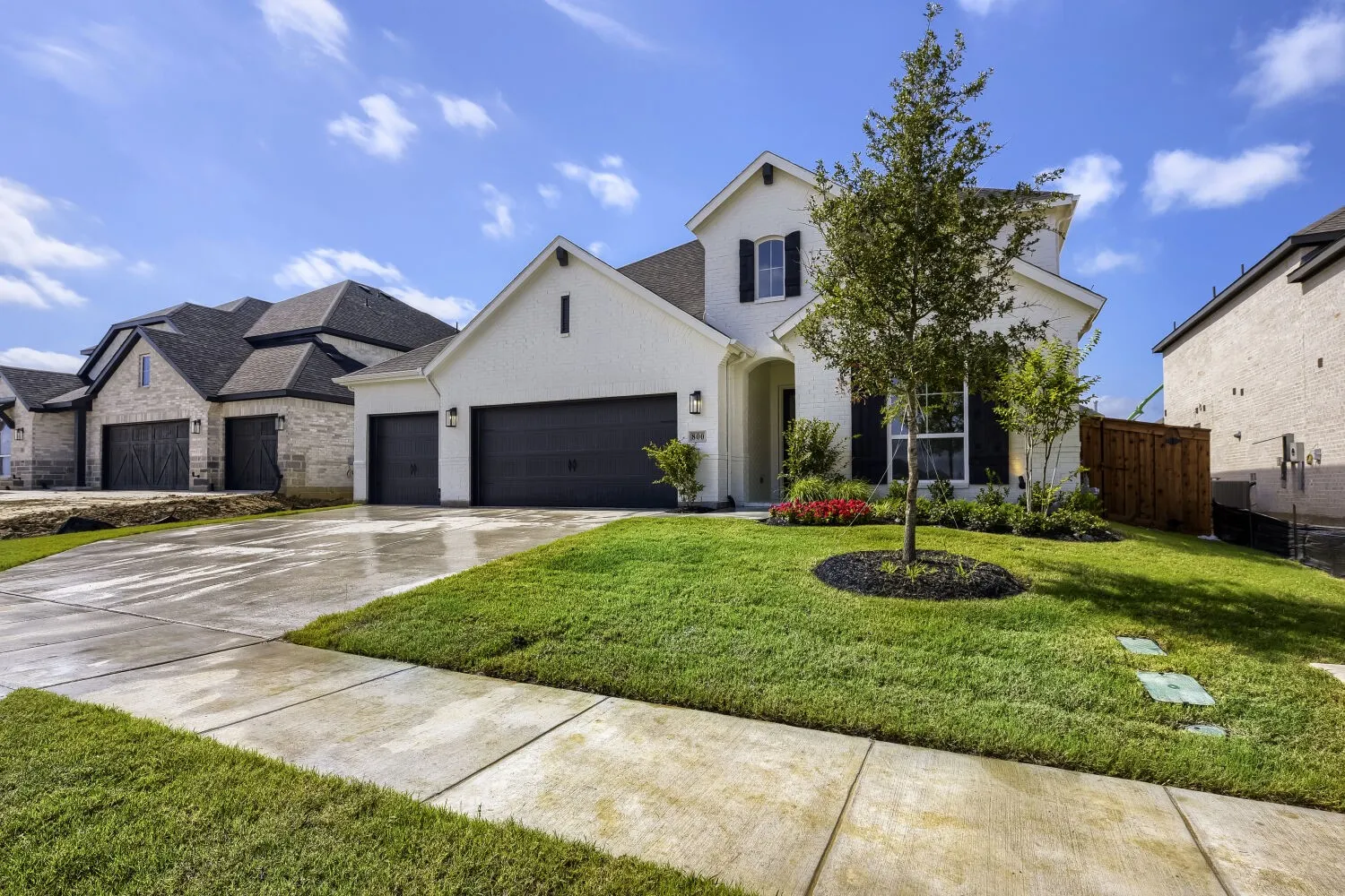 Modern white brick residence featuring a dark gray roof, black garage doors, and a manicured lawn