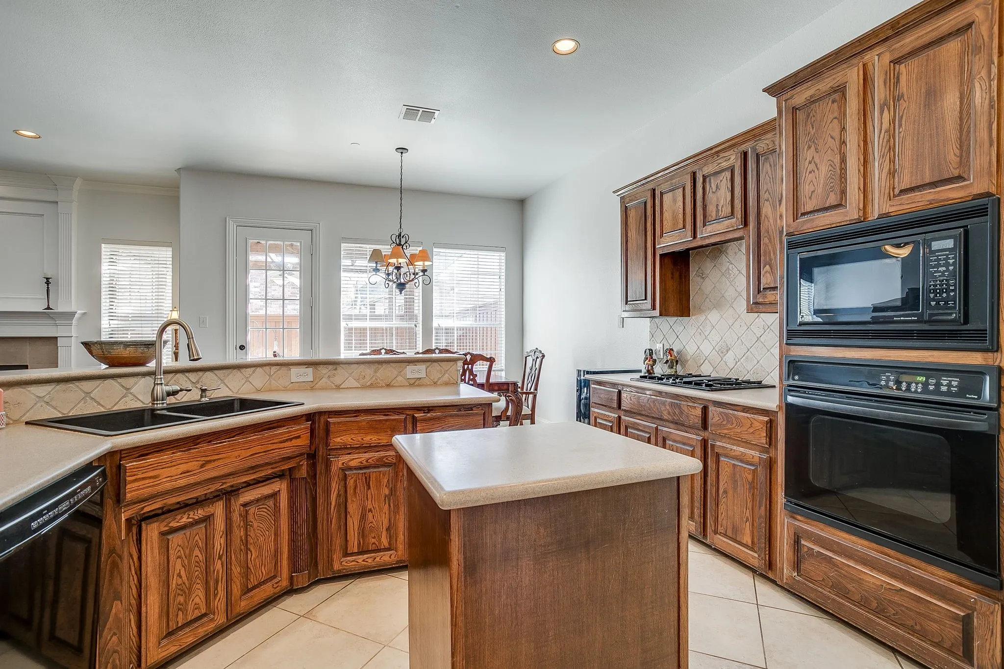 Kitchen featuring backsplash, black appliances, a chandelier, pendant lighting, and a center island