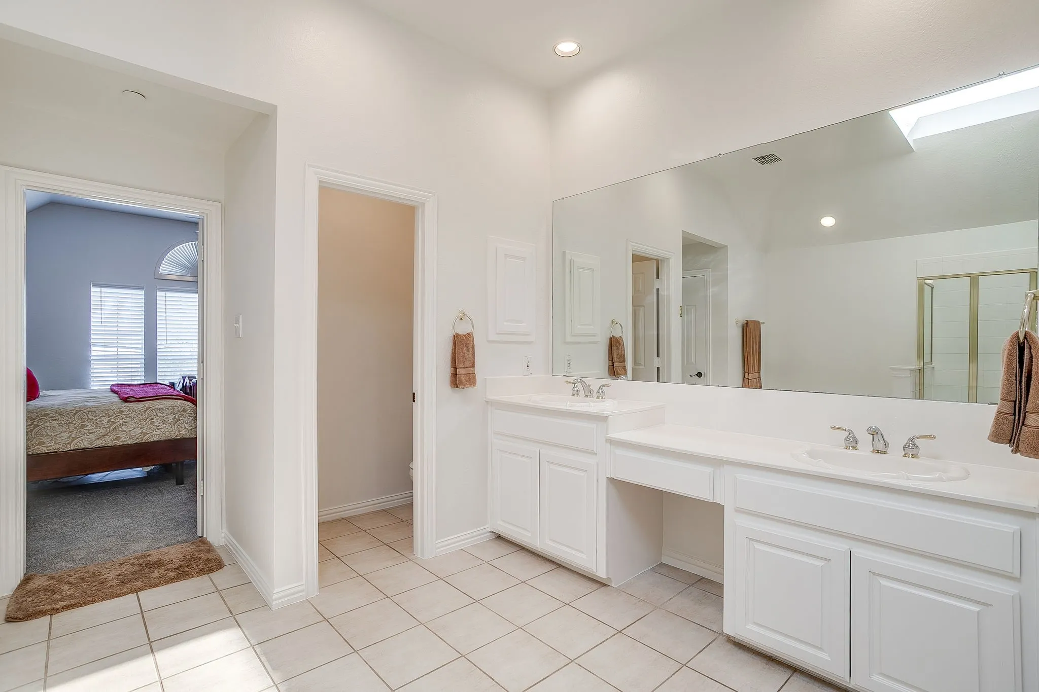 Ensuite bathroom featuring double vanity, a stall shower, light tile patterned floors, a skylight, and recessed lighting