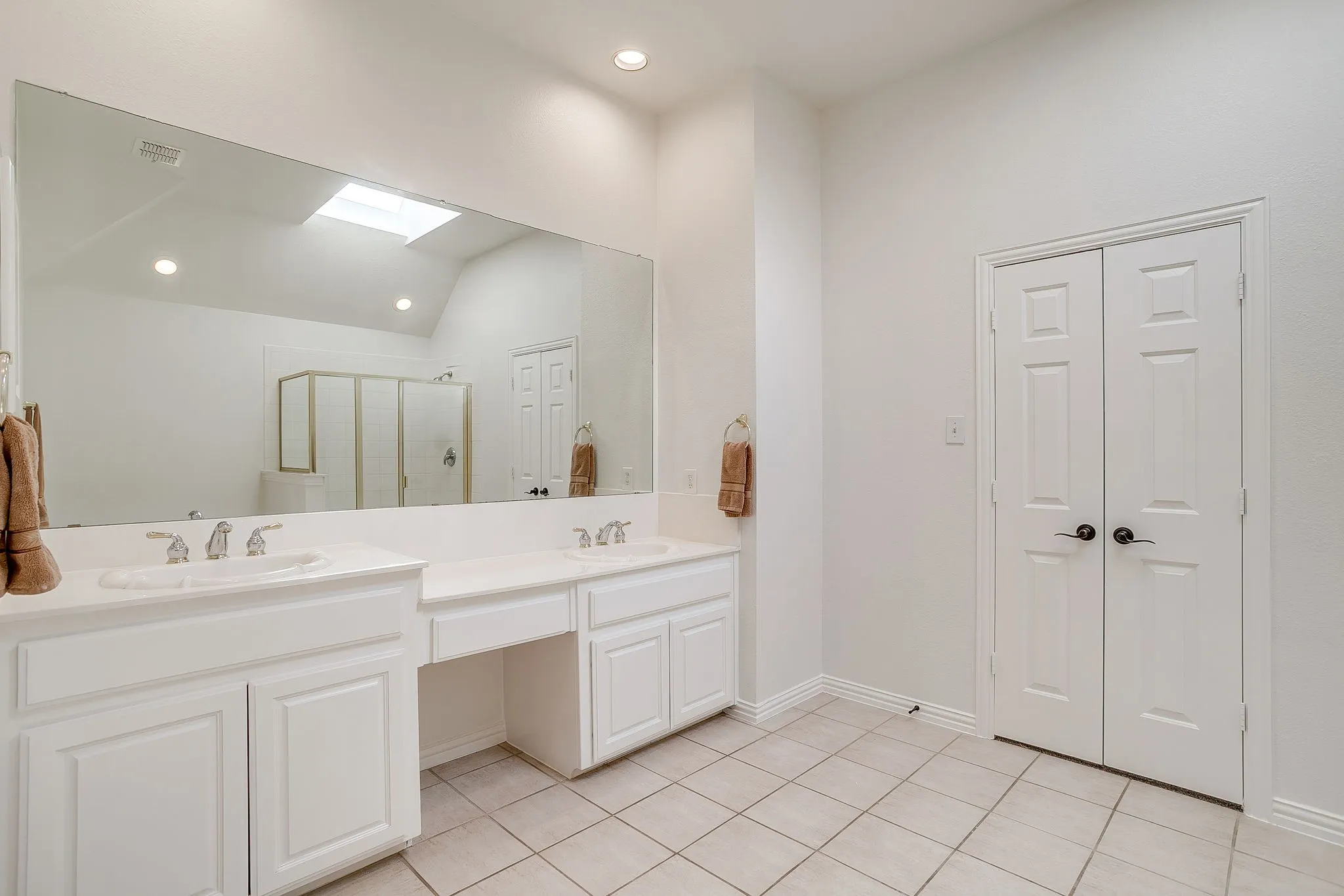 Bathroom featuring a skylight, a shower stall, double vanity, light tile patterned floors, and recessed lighting
