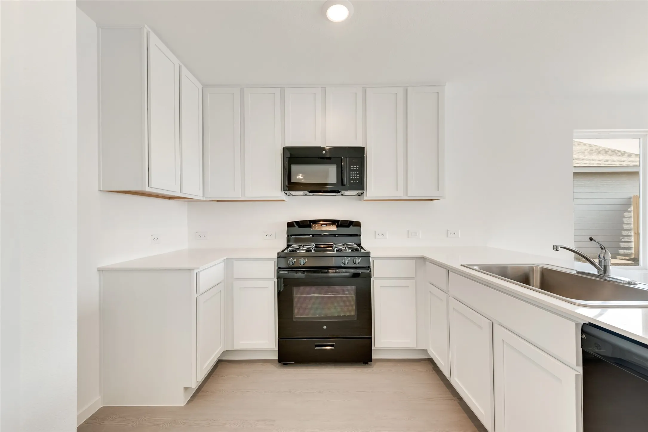 Kitchen with black appliances, white cabinetry, light wood-type flooring, and recessed lighting