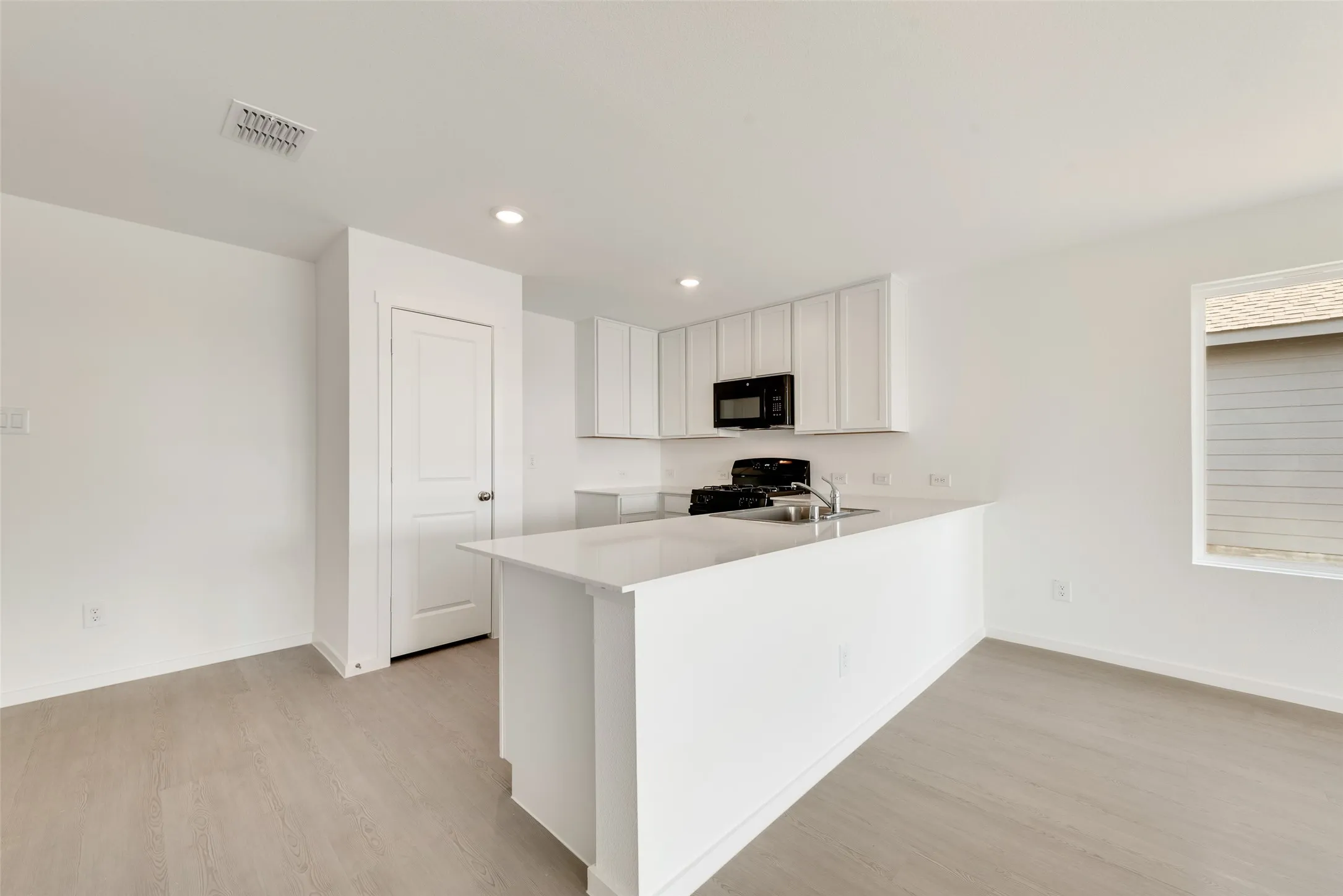Kitchen with white cabinetry, a peninsula, light wood-style floors, black appliances, and recessed lighting