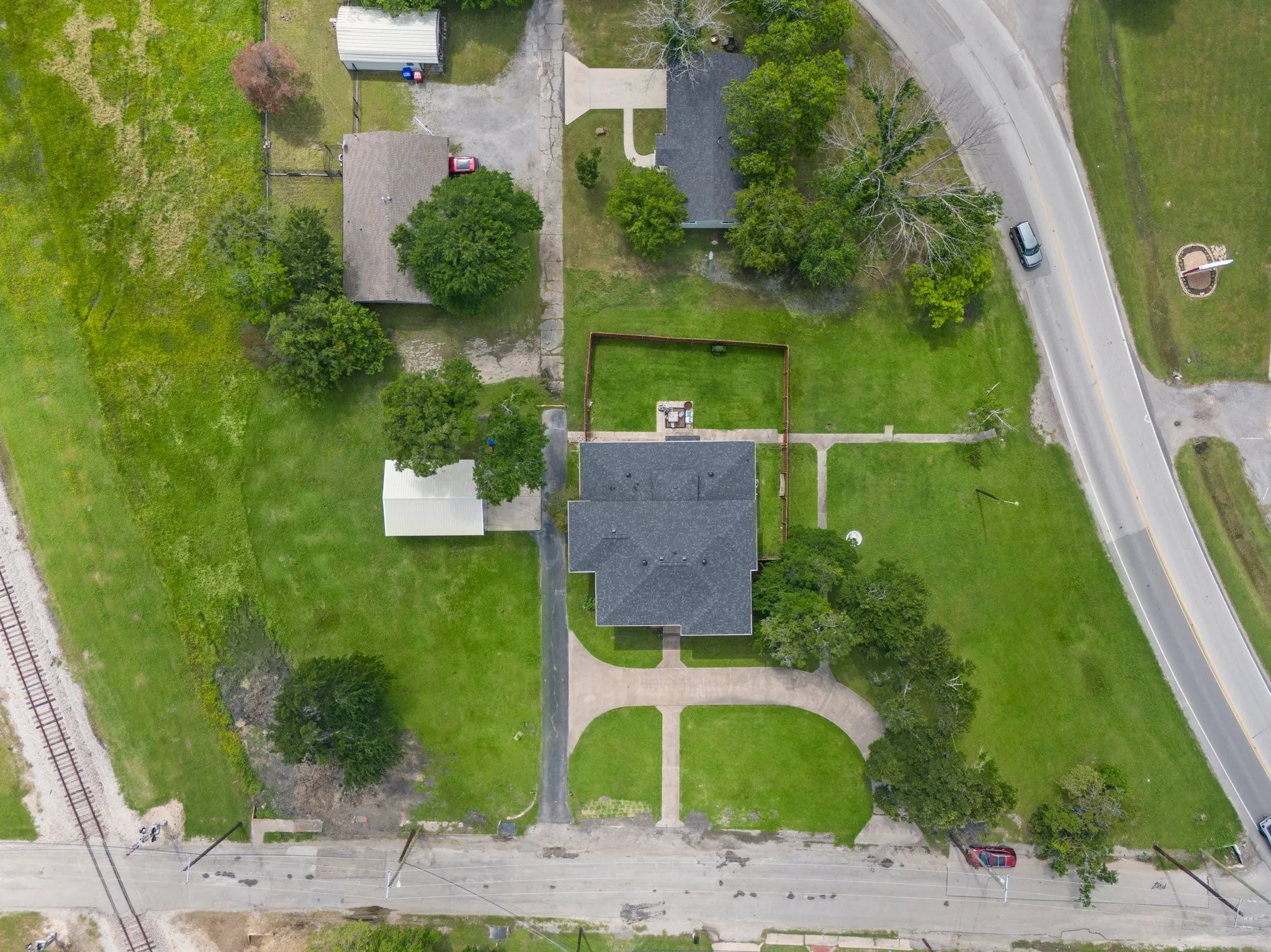 Expansive property featuring a circular driveway, mature trees, a private fenced yard area, and a dark shingle roof