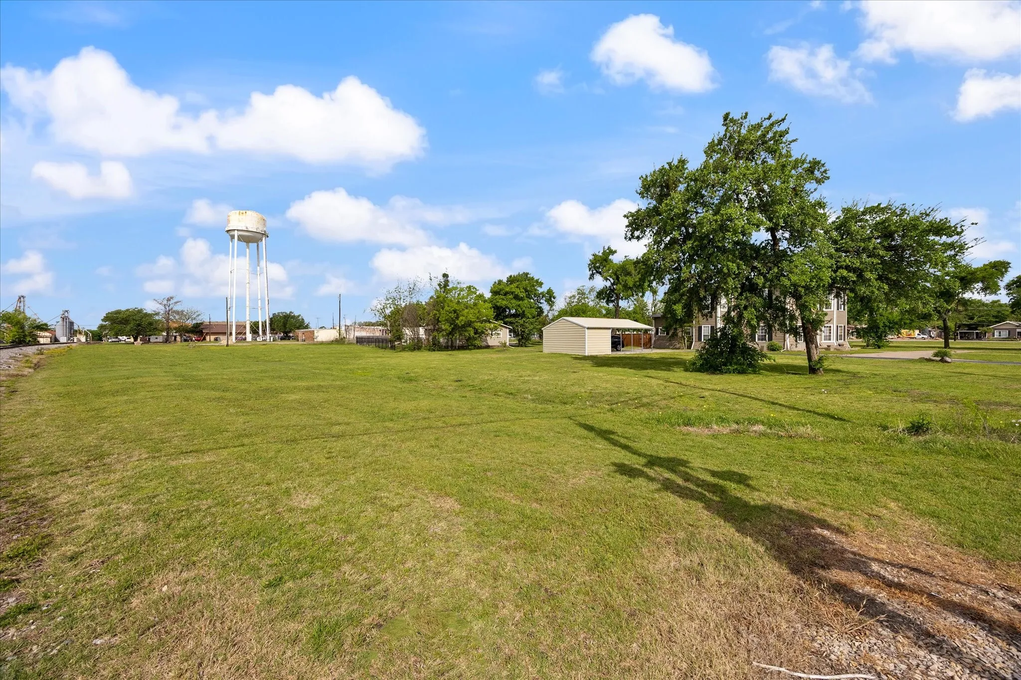 Expansive green space featuring mature trees and a metal storage building with a carport