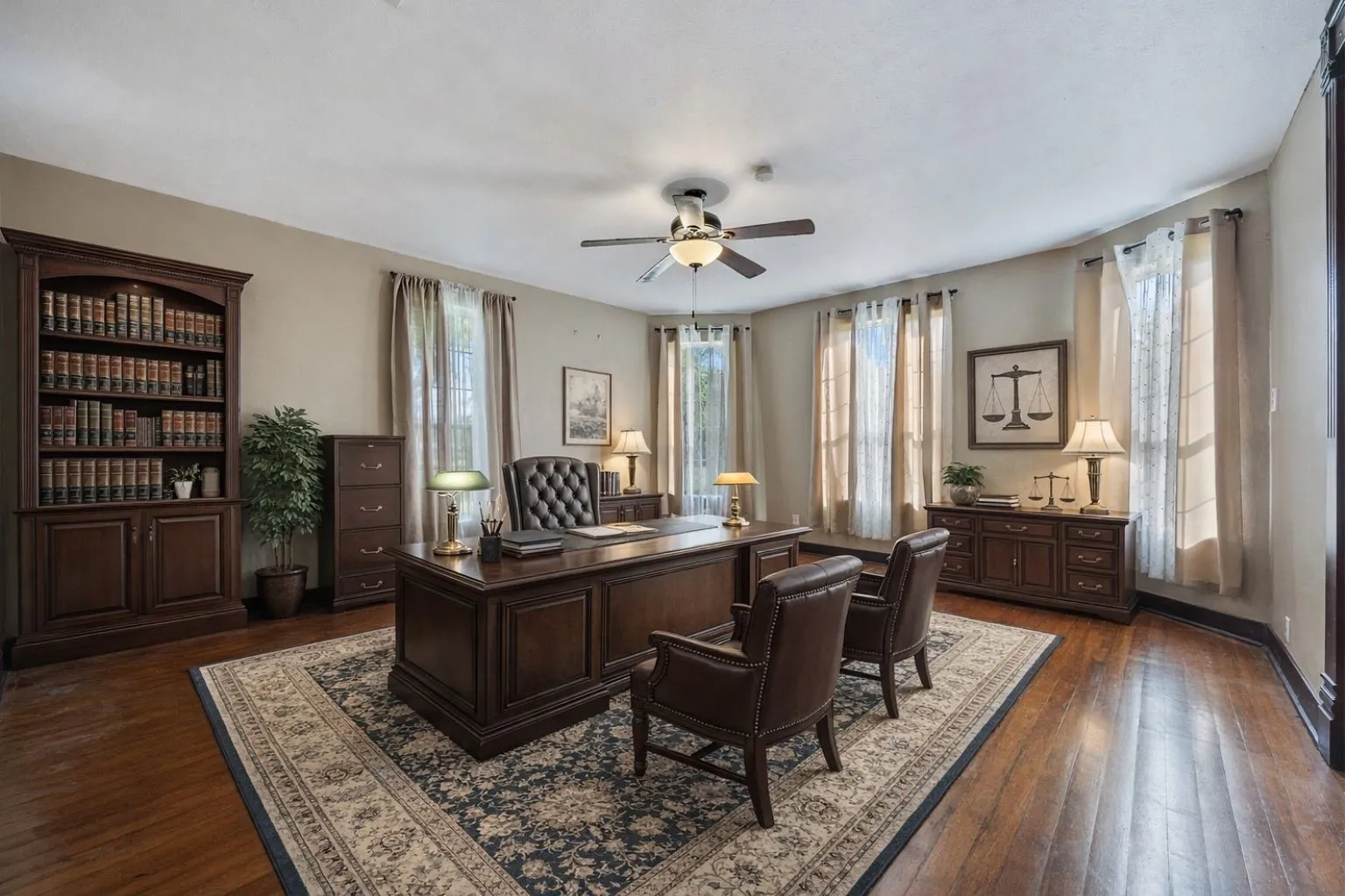 Hardwood flooring throughout this room featuring a ceiling fan with integrated lighting, multiple windows with neutral drapes, and a built-in wooden bookcase