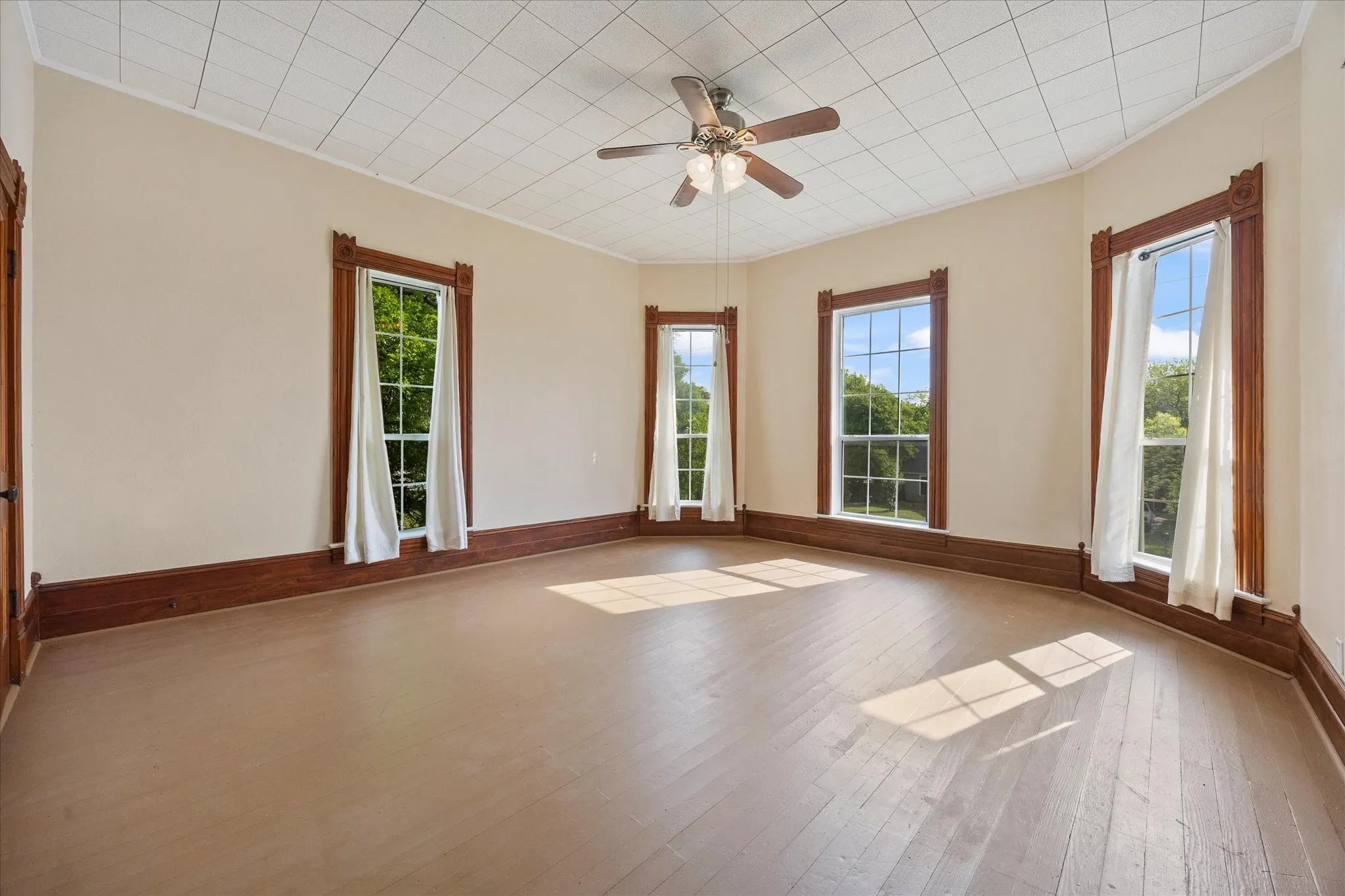 Room featuring wood-finish flooring, a ceiling fan, and multiple windows with detailed wood trim