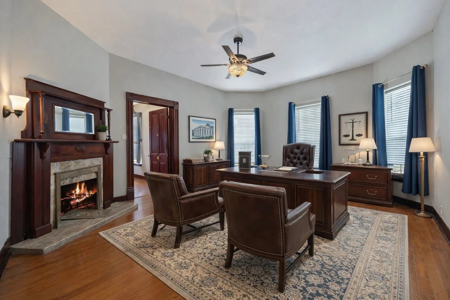 Room featuring hardwood flooring, a decorative fireplace with a wood mantle and stone surround, and a ceiling fan with integrated lighting