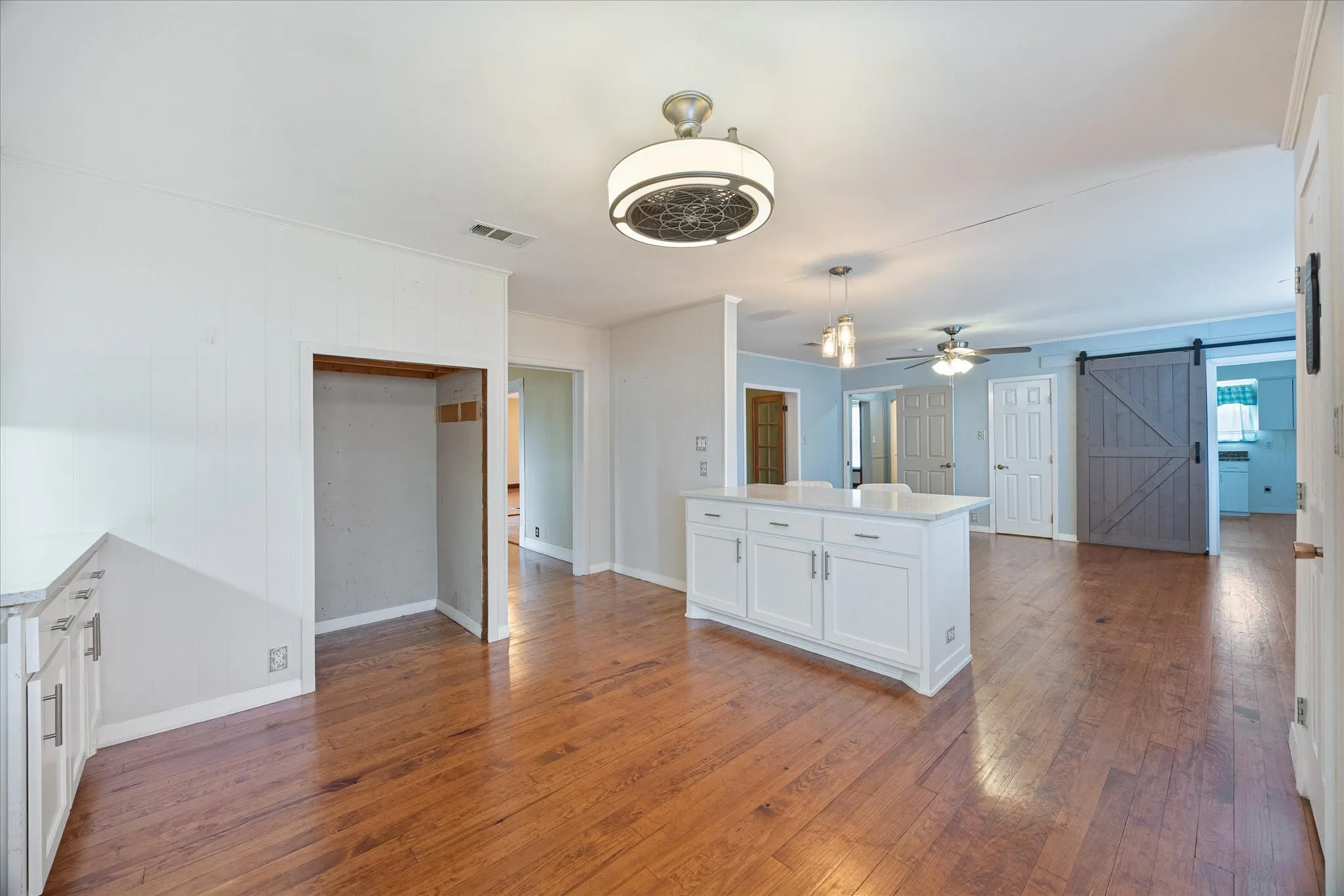 Spacious open-concept interior featuring wood-finish flooring, a central island with white cabinetry and a light-toned countertop, and multiple ceiling fans
