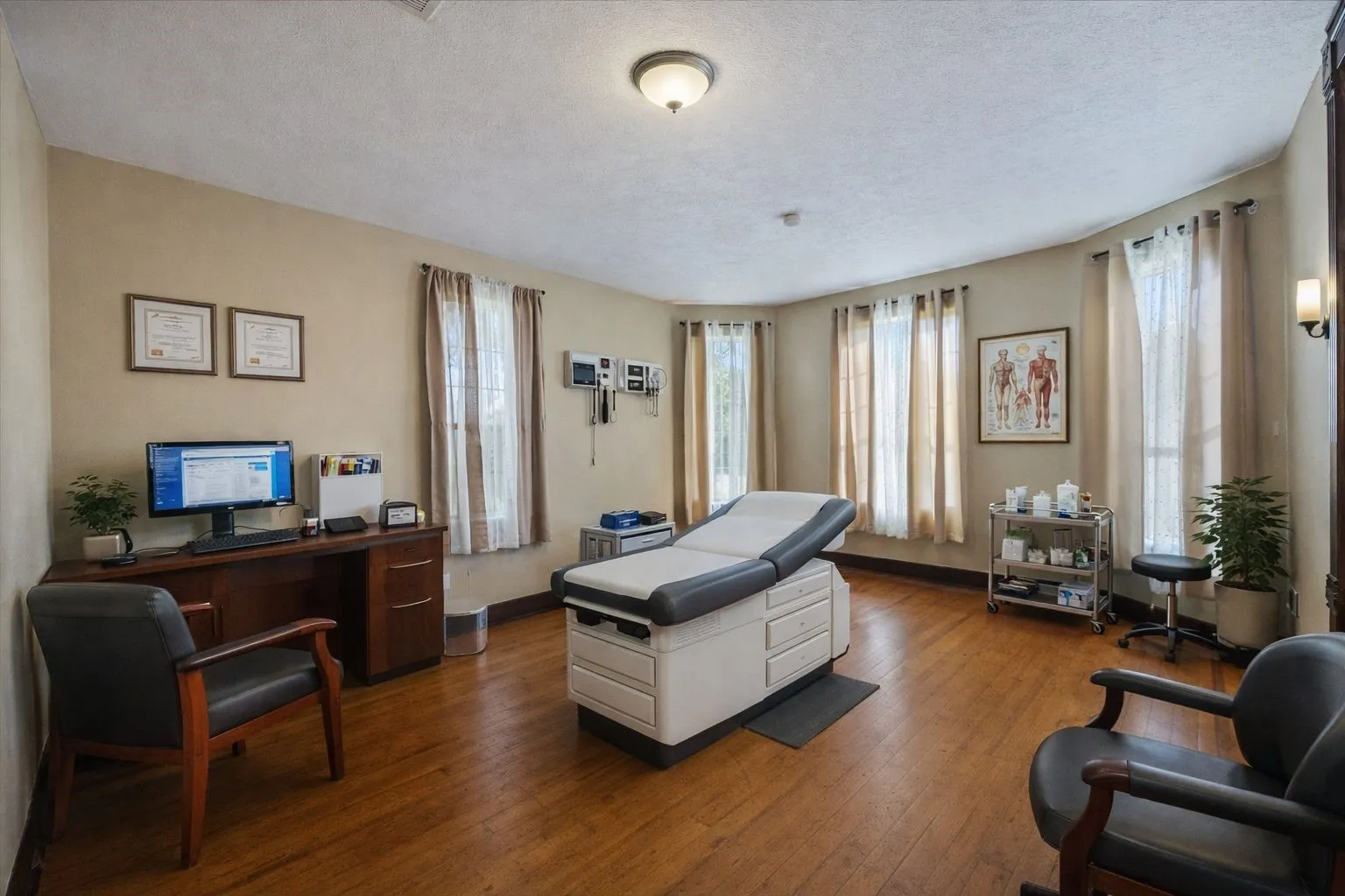 Spacious room with wood-finish flooring, multiple windows, and a built-in wall sconce