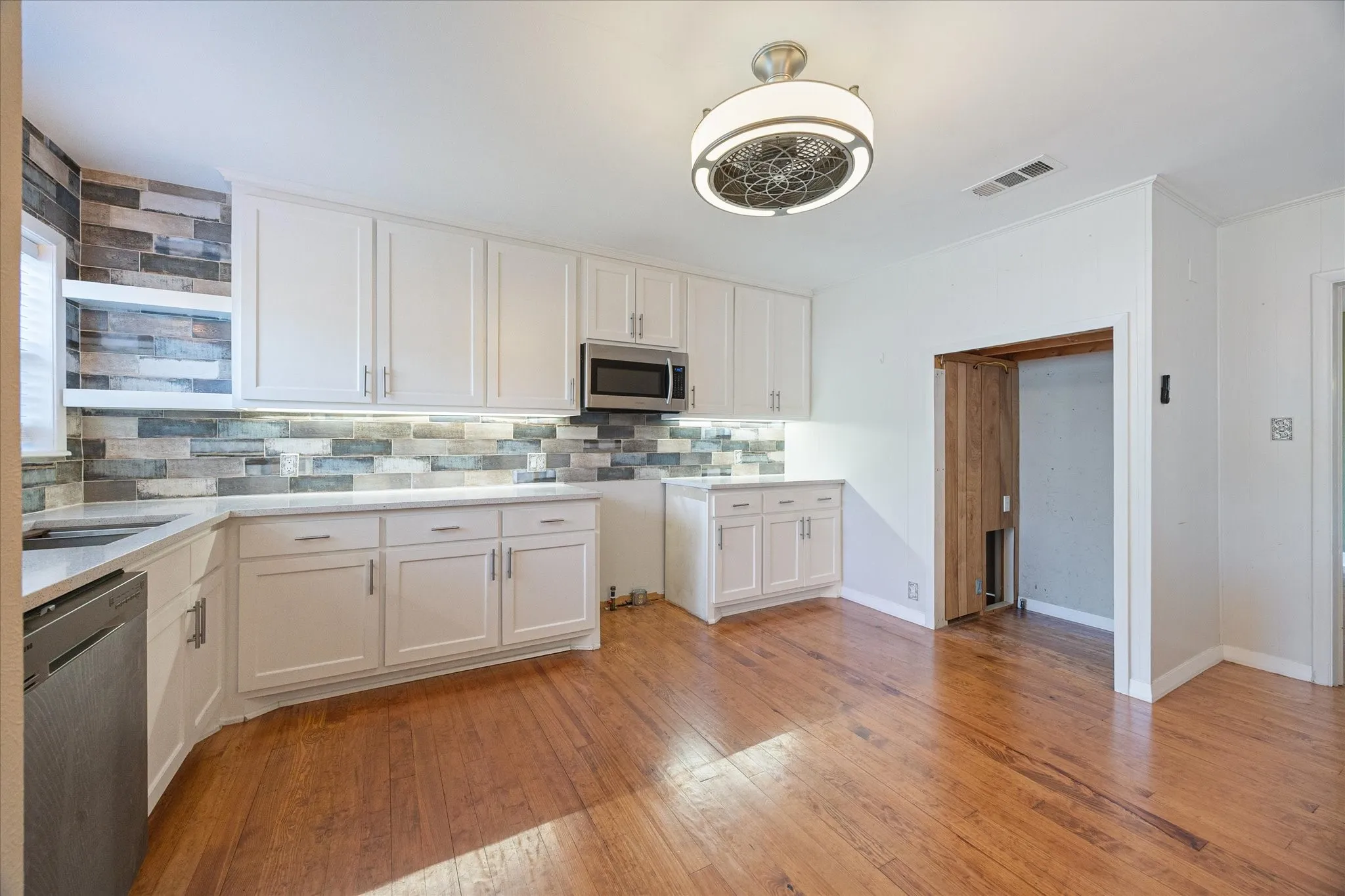 Well-appointed kitchen featuring white cabinetry, light-toned countertops, a full mosaic tile backsplash, and wood-finish flooring