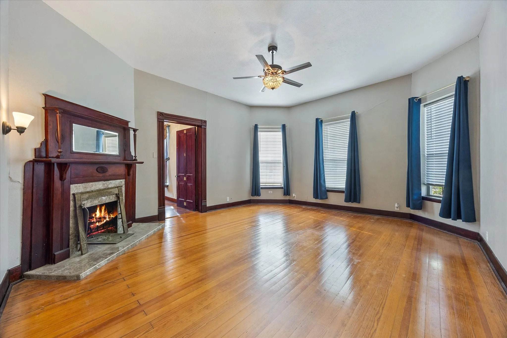 Spacious room featuring wood-finish flooring, a detailed wooden fireplace surround with a stone hearth, and a ceiling fan with integrated lighting