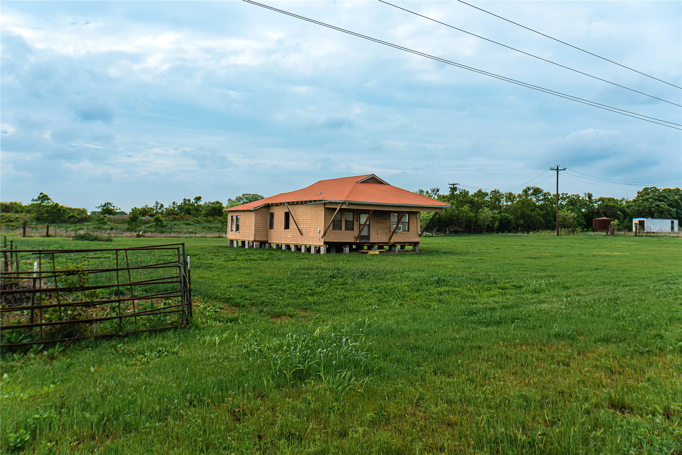 Single-story residential structure on raised piers featuring an orange-tiled roof and unfinished exterior siding