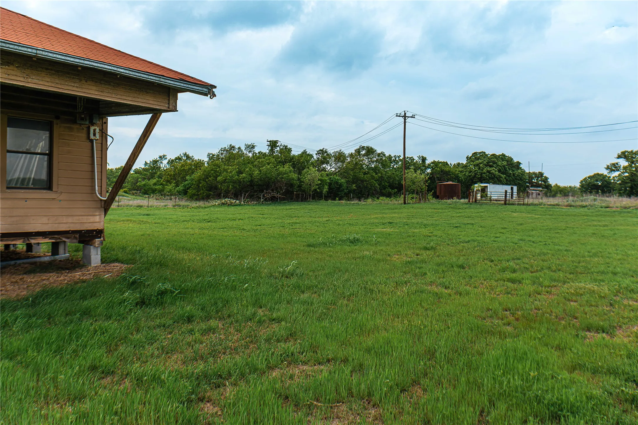 Expansive green space featuring a building with wood siding and a red roof, elevated on concrete blocks
