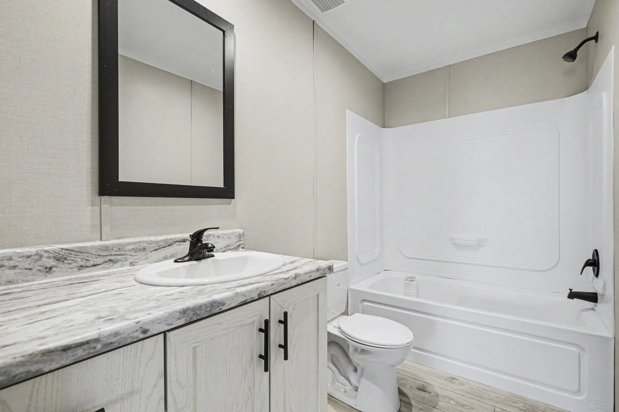 Full bathroom featuring a white vanity with a lovely countertop, integrated china sink, black framed mirror and matte black faucet - upgrades for an aesthetic you will love.