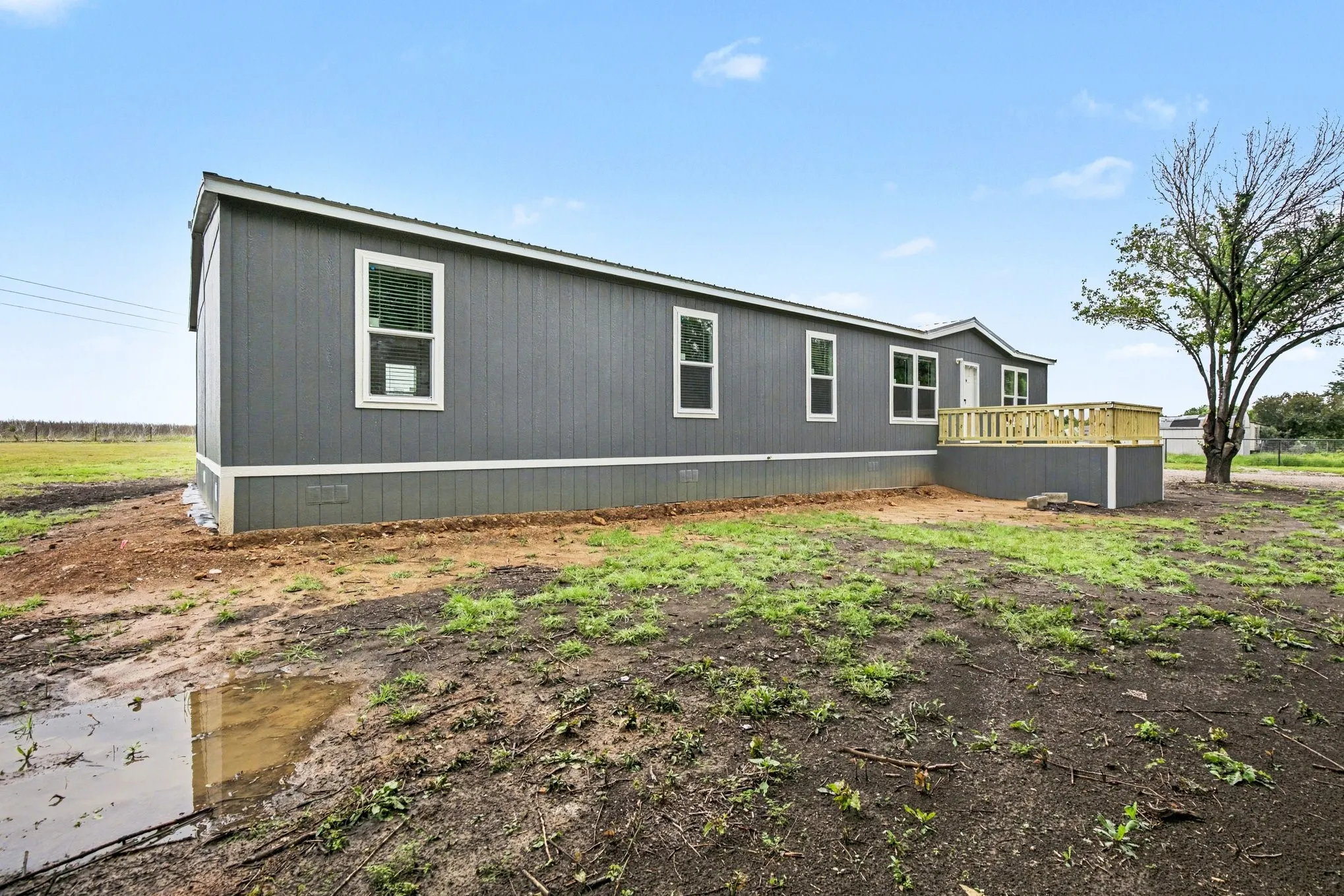Contemporary single-story residence with a dark blue-gray exterior, white trim, multiple windows, and a newly constructed wooden deck