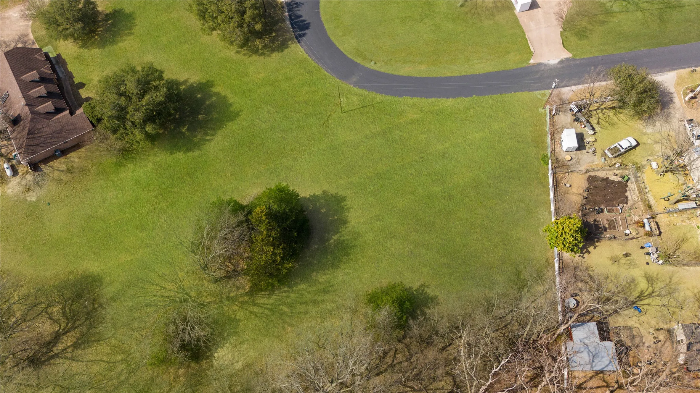 Expansive green lot featuring mature trees and a paved road
