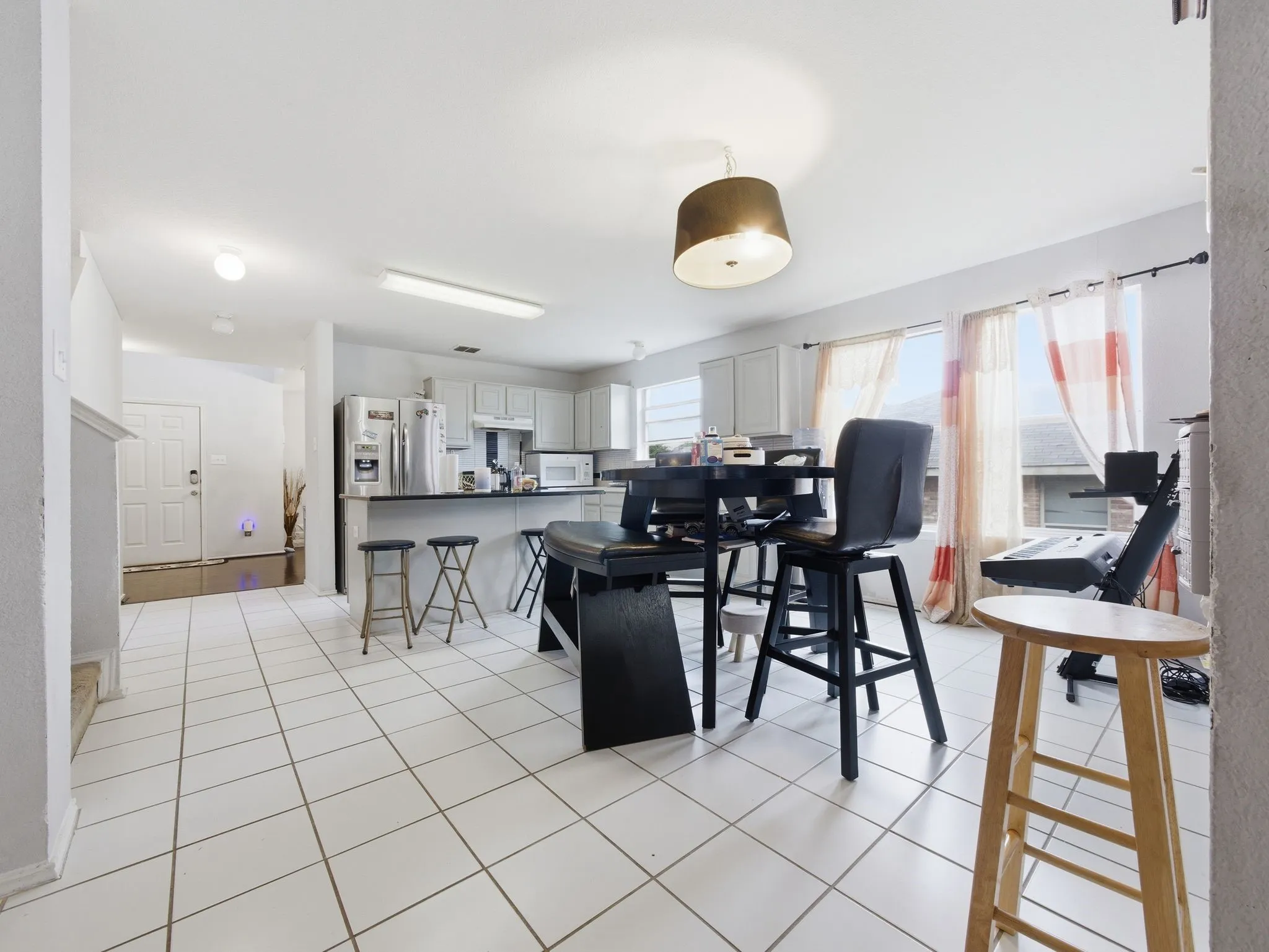 Open-concept kitchen and dining area featuring white tile flooring, light-toned cabinetry, a breakfast bar, and multiple windows