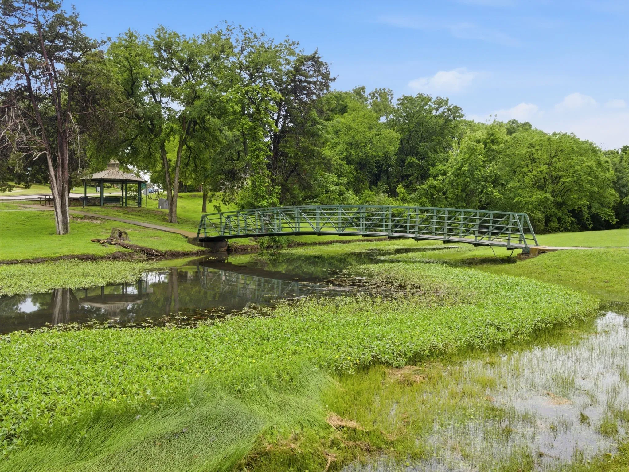 Green metal pedestrian bridge spanning a tranquil water feature