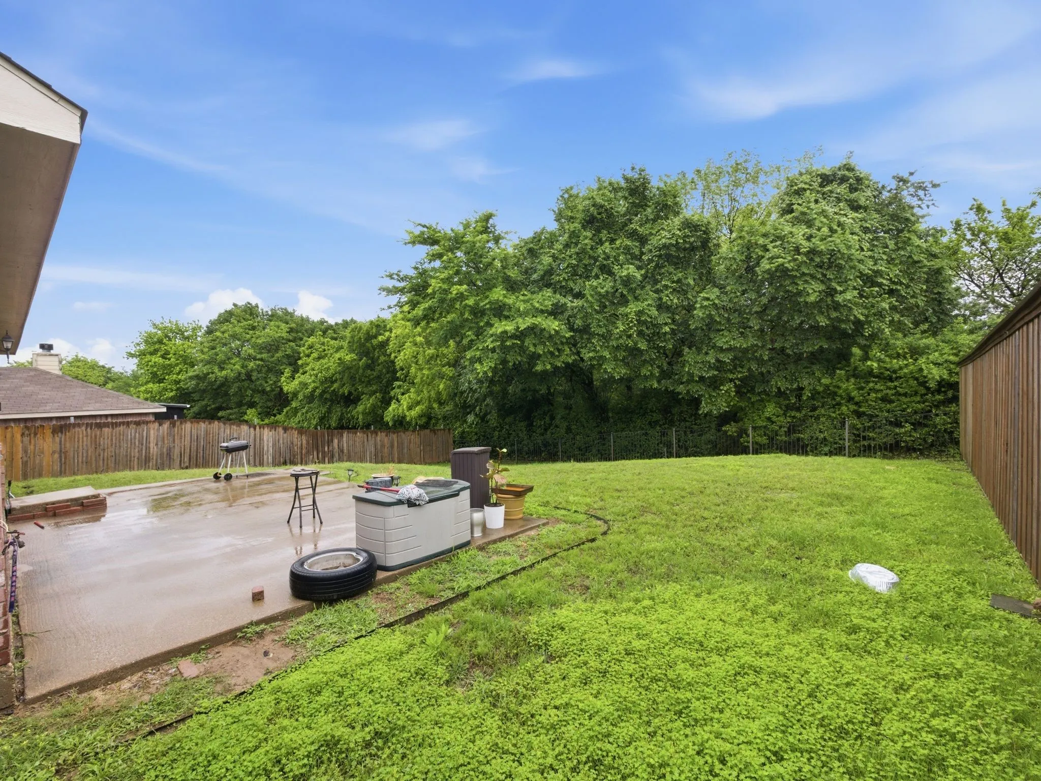 Expansive backyard featuring a large concrete patio, a privacy fence, and a generous lawn area bordered by mature trees