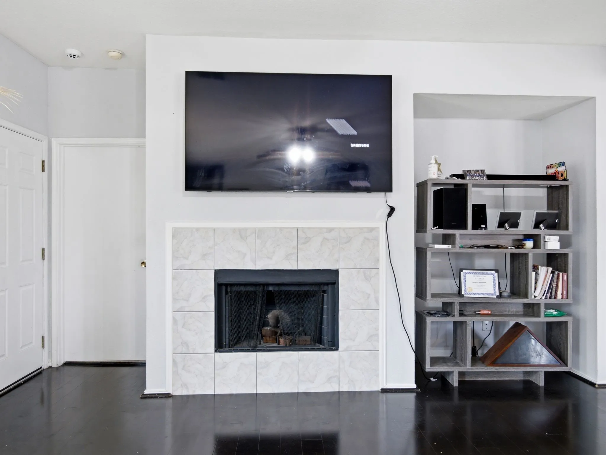 Living area featuring a fireplace with a light-colored tile surround, dark wood-finish flooring, and a recessed shelving unit