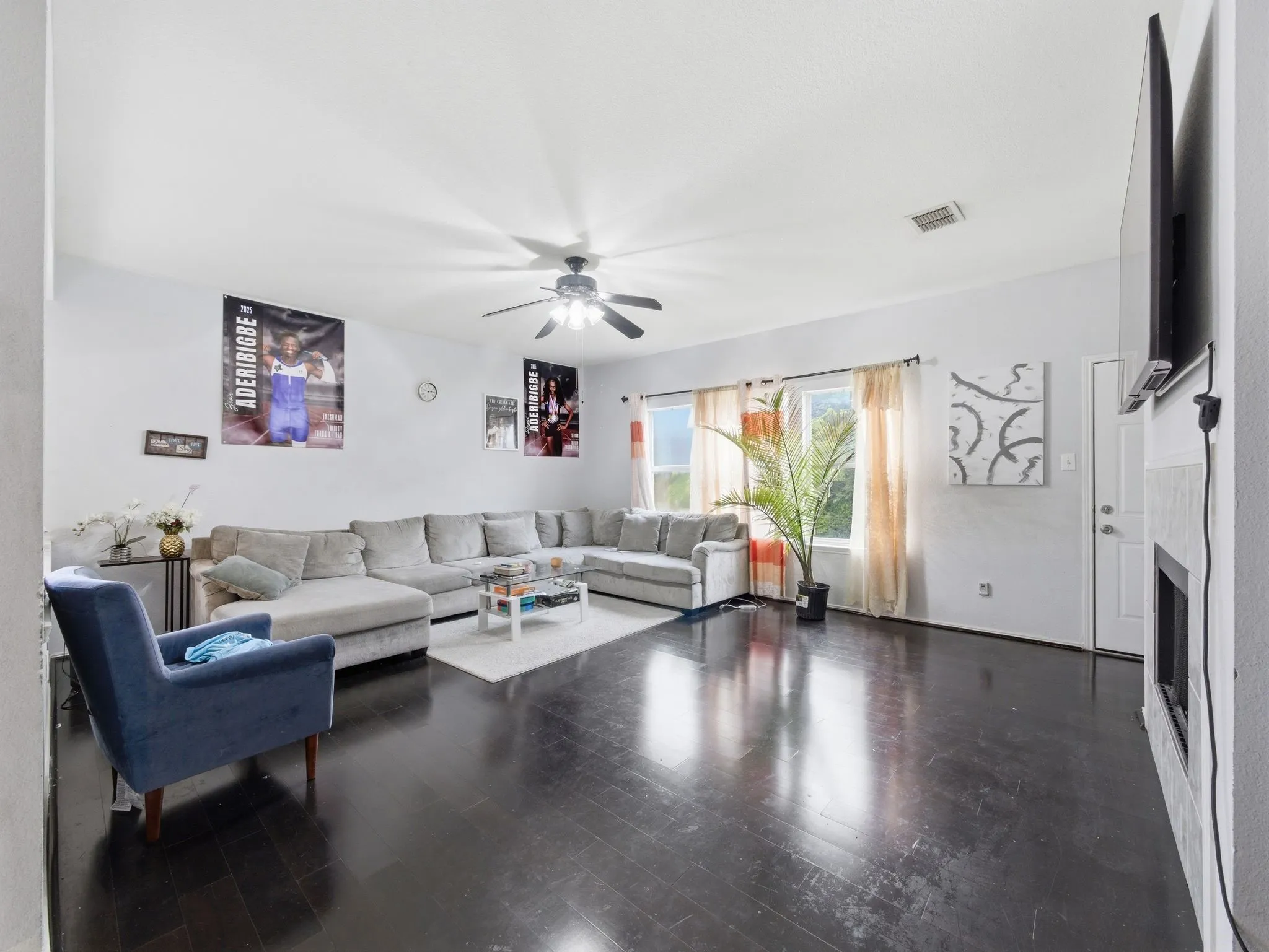 Spacious living area featuring dark wood-finish flooring, a white ceiling with a ceiling fan, and multiple windows with vertical blinds