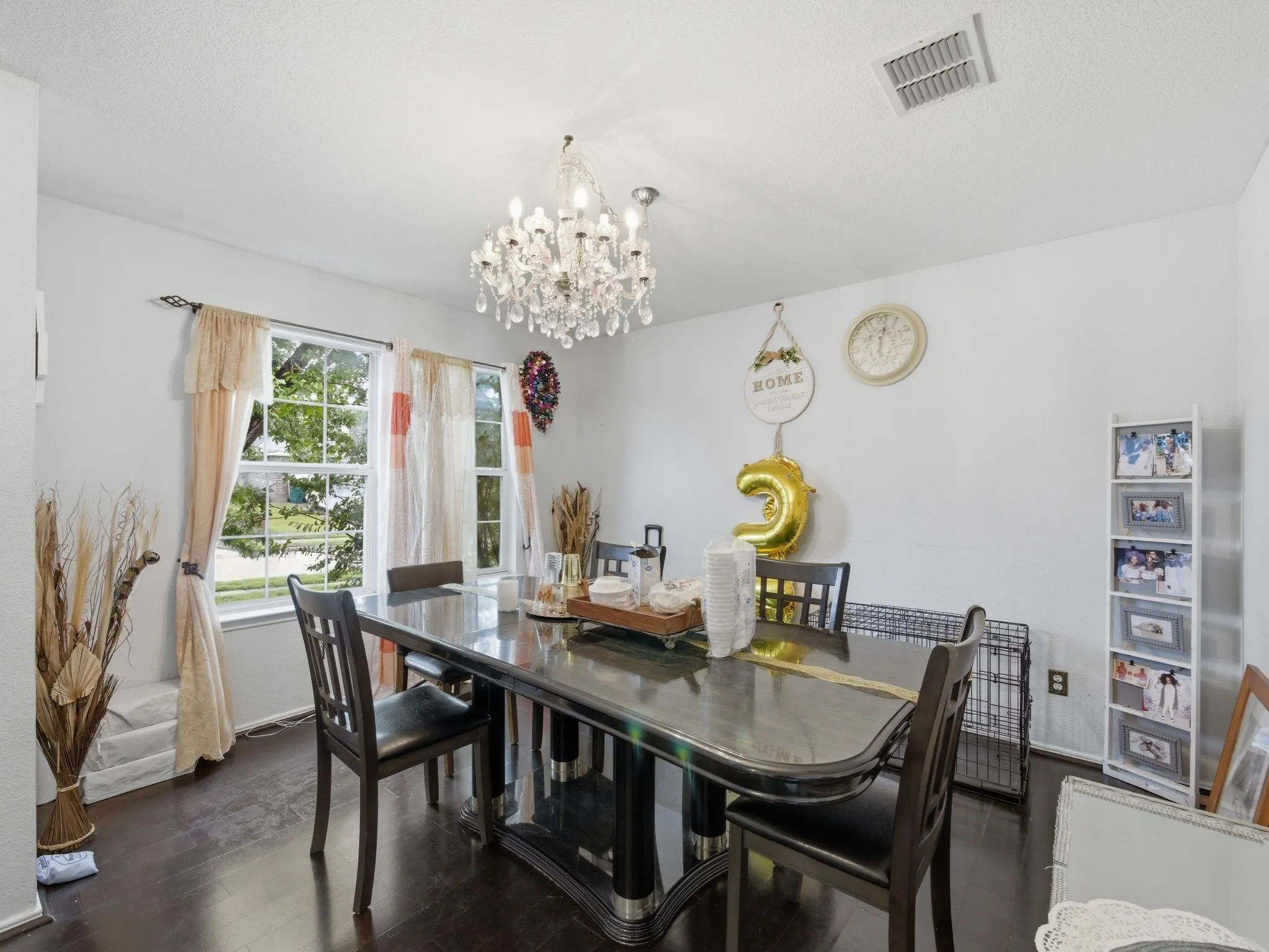 Dining area featuring a prominent chandelier, dark wood-finish flooring, and natural light from a window with white trim