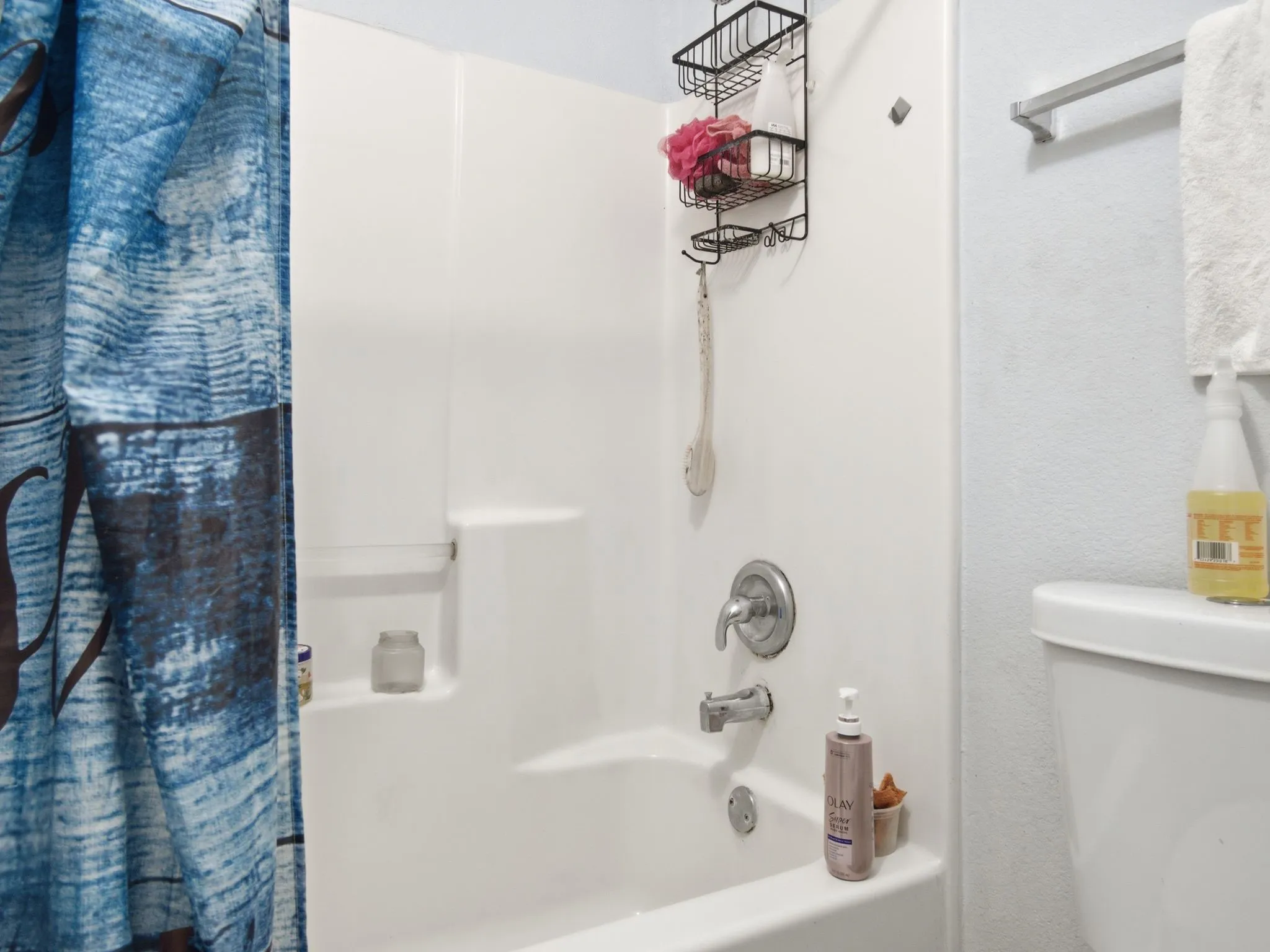 White shower-over-tub combination with built-in shelving, chrome fixtures, and a white toilet