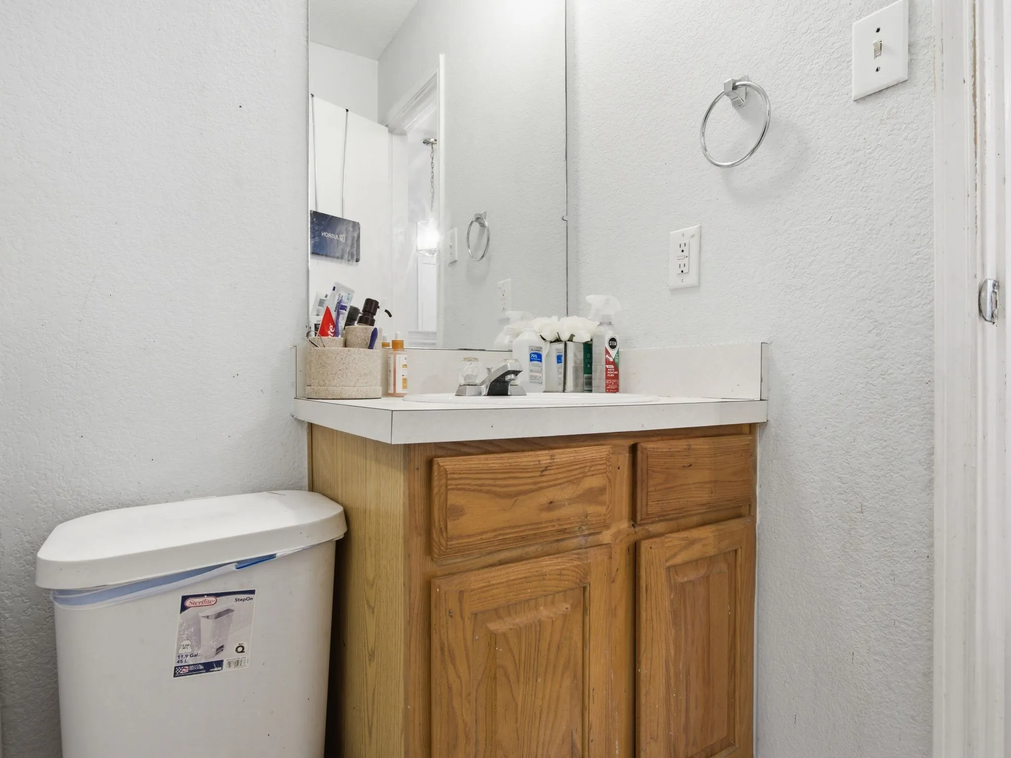 Bathroom featuring a wood-finish vanity with cabinet storage, a light-toned countertop, and a wall-mounted mirror