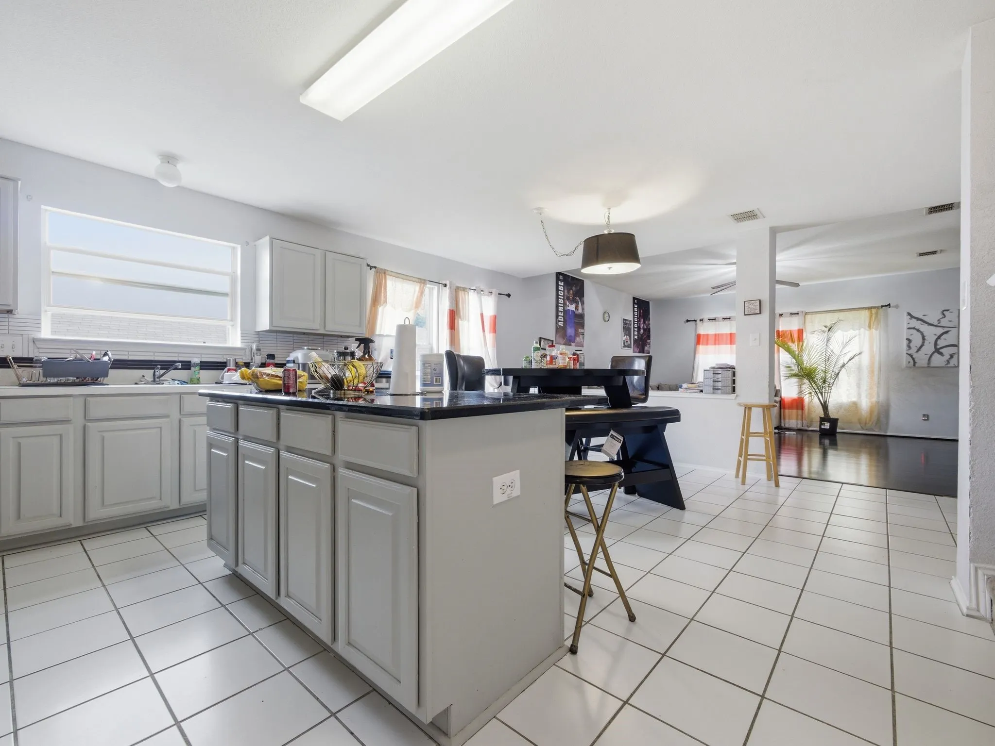 Kitchen featuring a central island with a dark countertop, white tile flooring, light-toned cabinetry, and a fluorescent ceiling light fixture