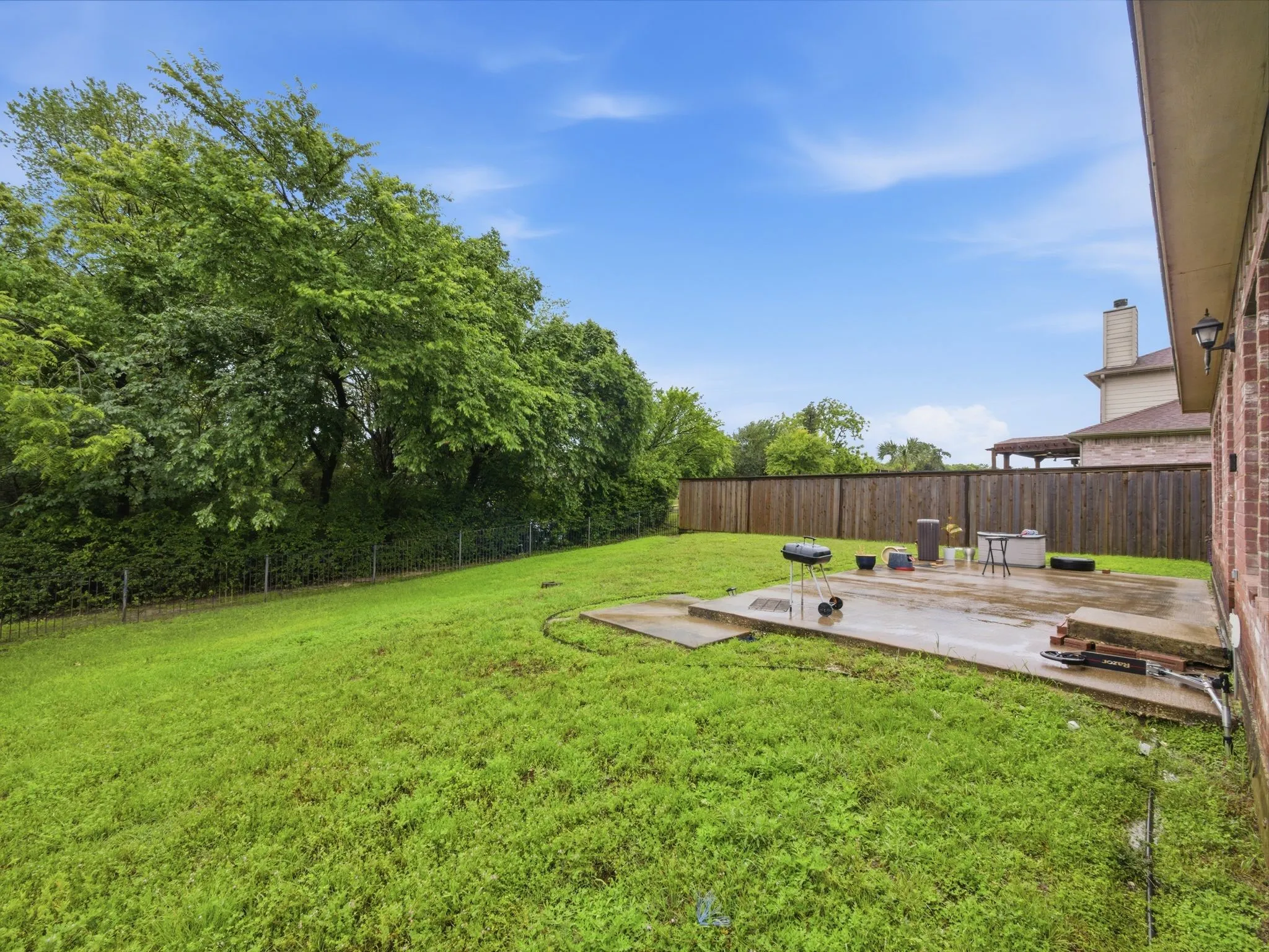 Expansive backyard featuring a large concrete patio, a privacy fence, and mature trees along the perimeter