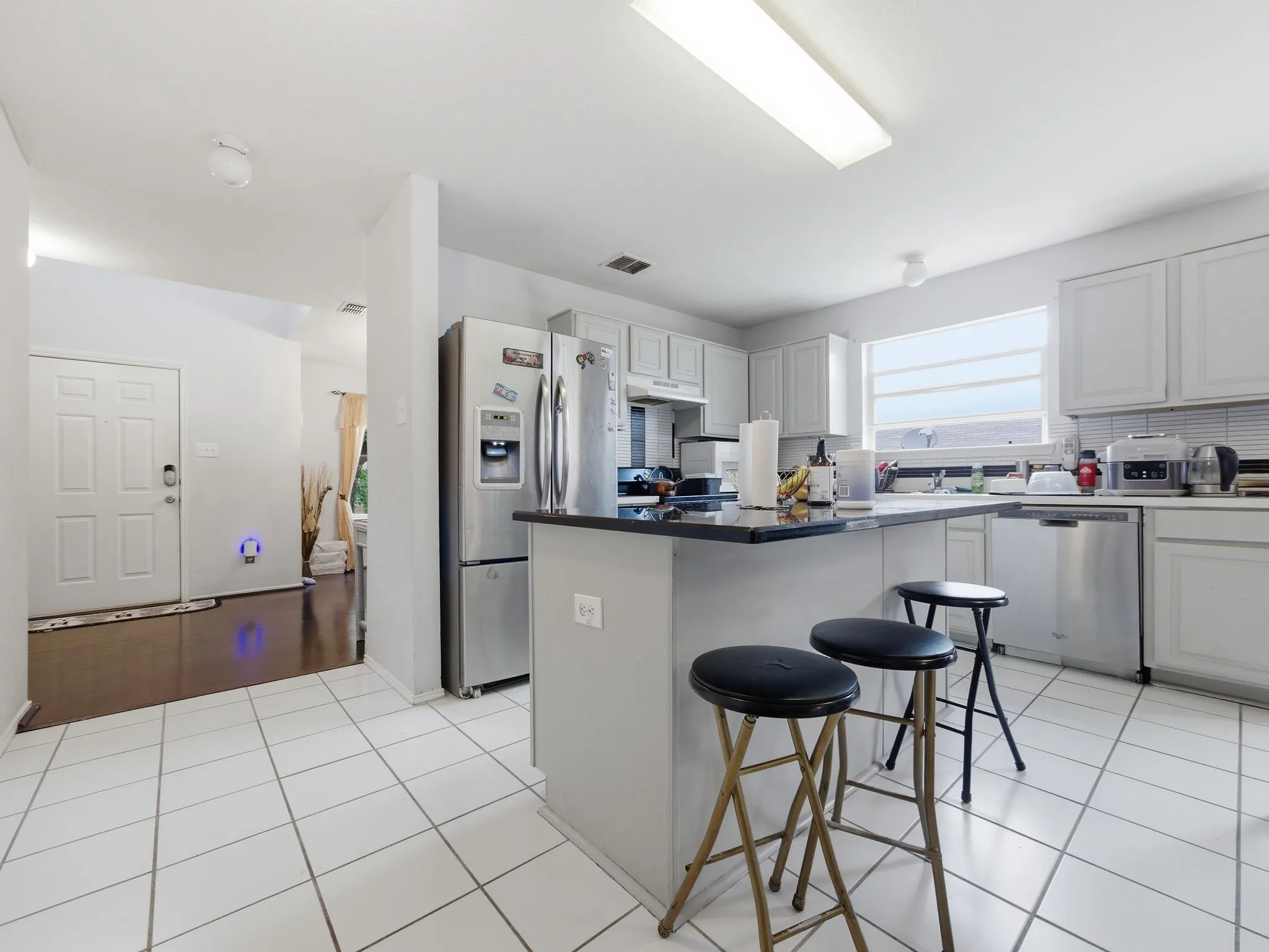 Kitchen featuring a central island with a dark countertop, white cabinetry, stainless steel appliances, and white square tile flooring