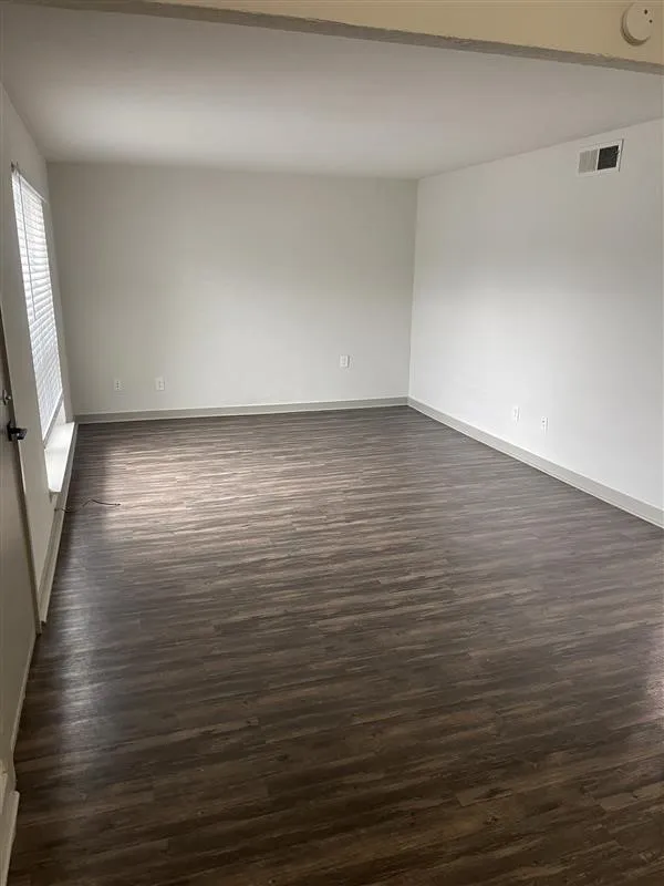 Spacious room featuring wood-finish flooring, white walls, and a window with blinds