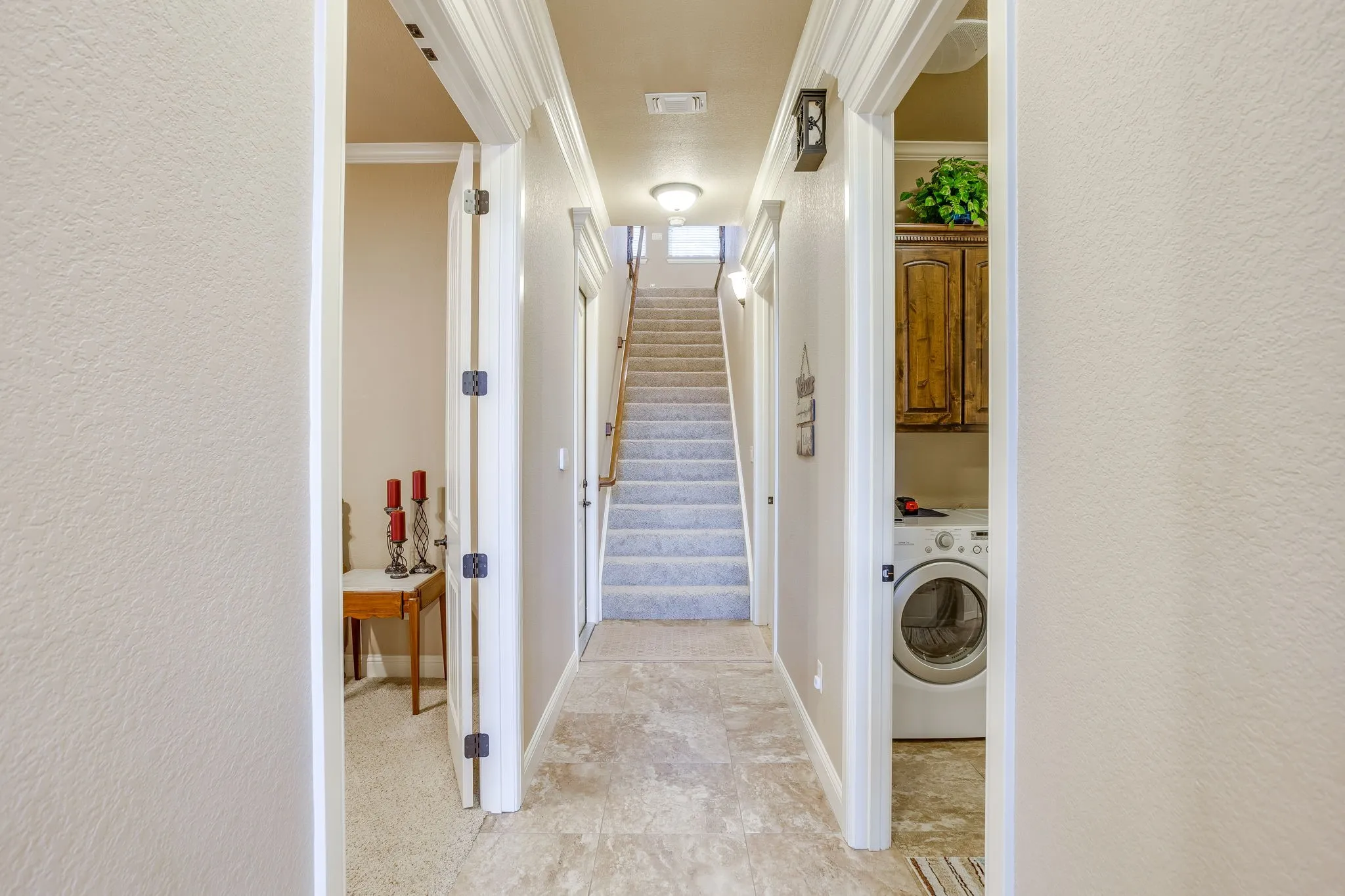 Hallway leading to primary bedroom, guest or office room, utility/full bathroom area and staircase to upstairs rooms.