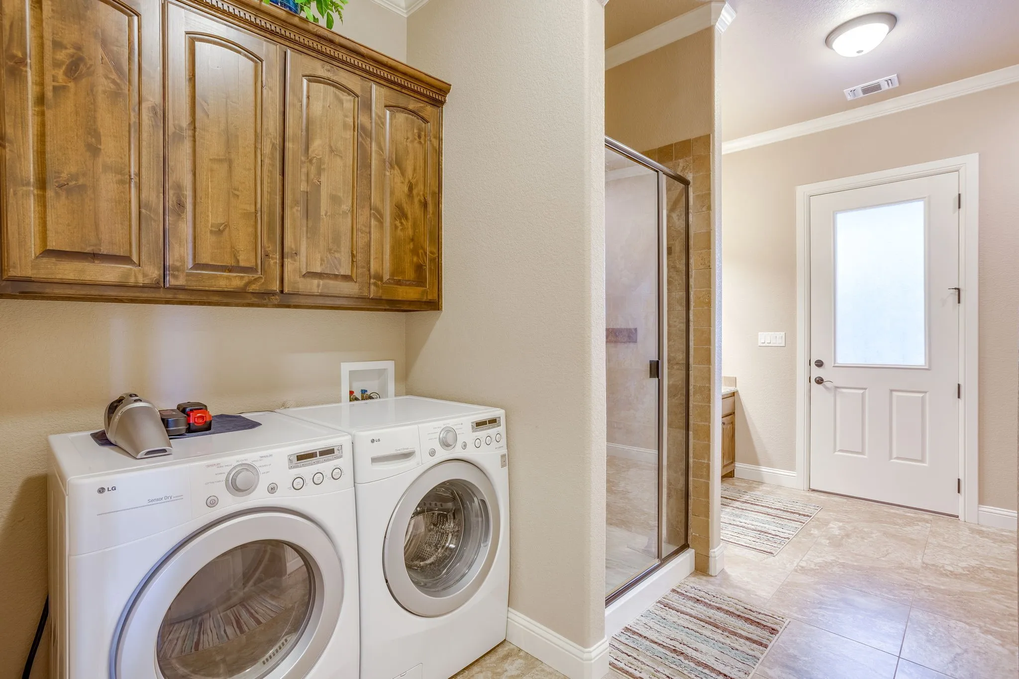 Utility area featuring wood cabinetry, tiled flooring, glass-enclosed shower, and a frosted glass panel door