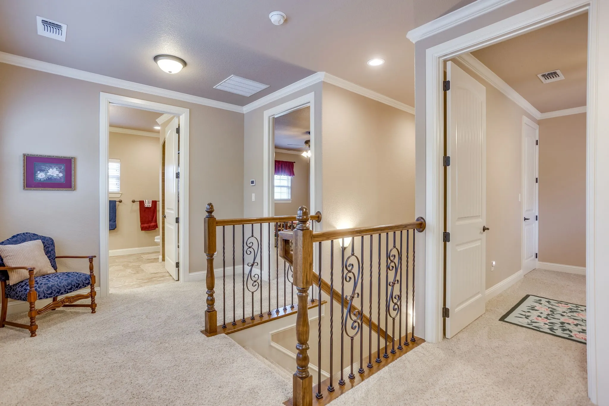 Carpeted hallway featuring a wooden handrail with decorative wrought iron balusters, crown molding, and recessed lighting