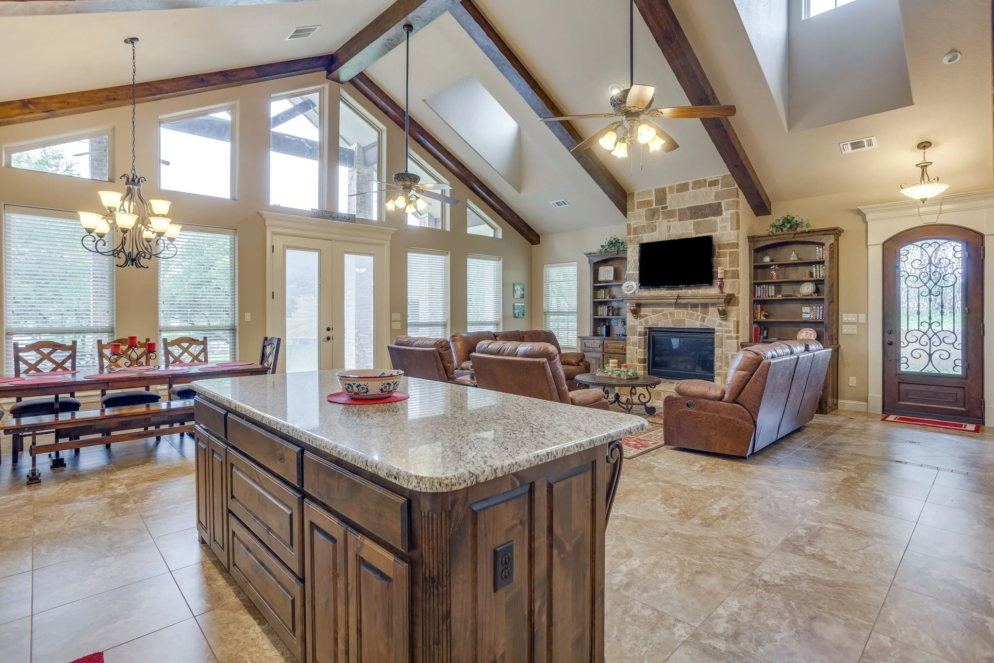 Spacious open-concept interior featuring a kitchen island with stone countertop, tile flooring, and vaulted ceilings with exposed wood beams
