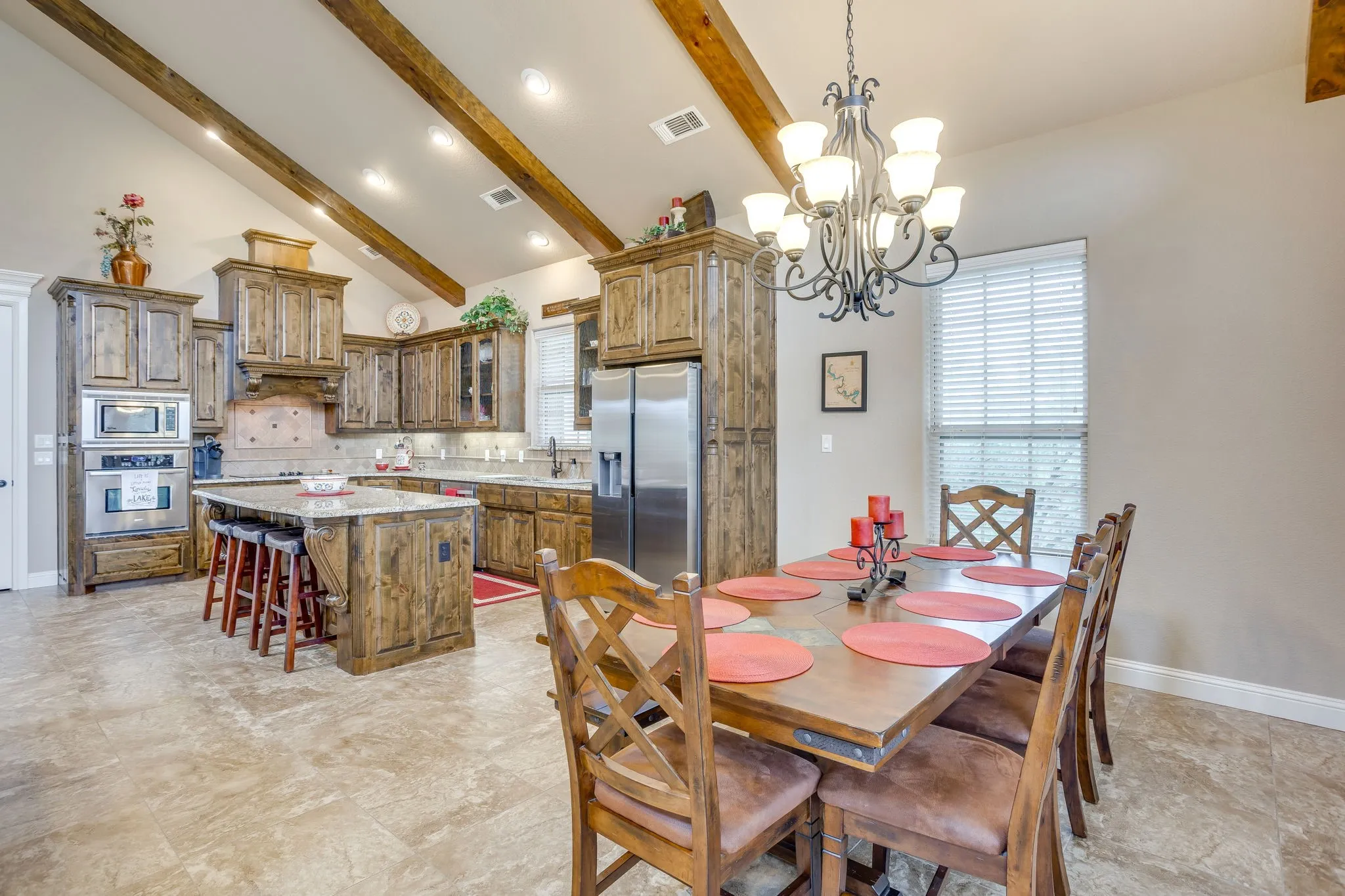 Kitchen and dining area featuring vaulted ceilings with exposed wood beams, recessed lighting, and a chandelier