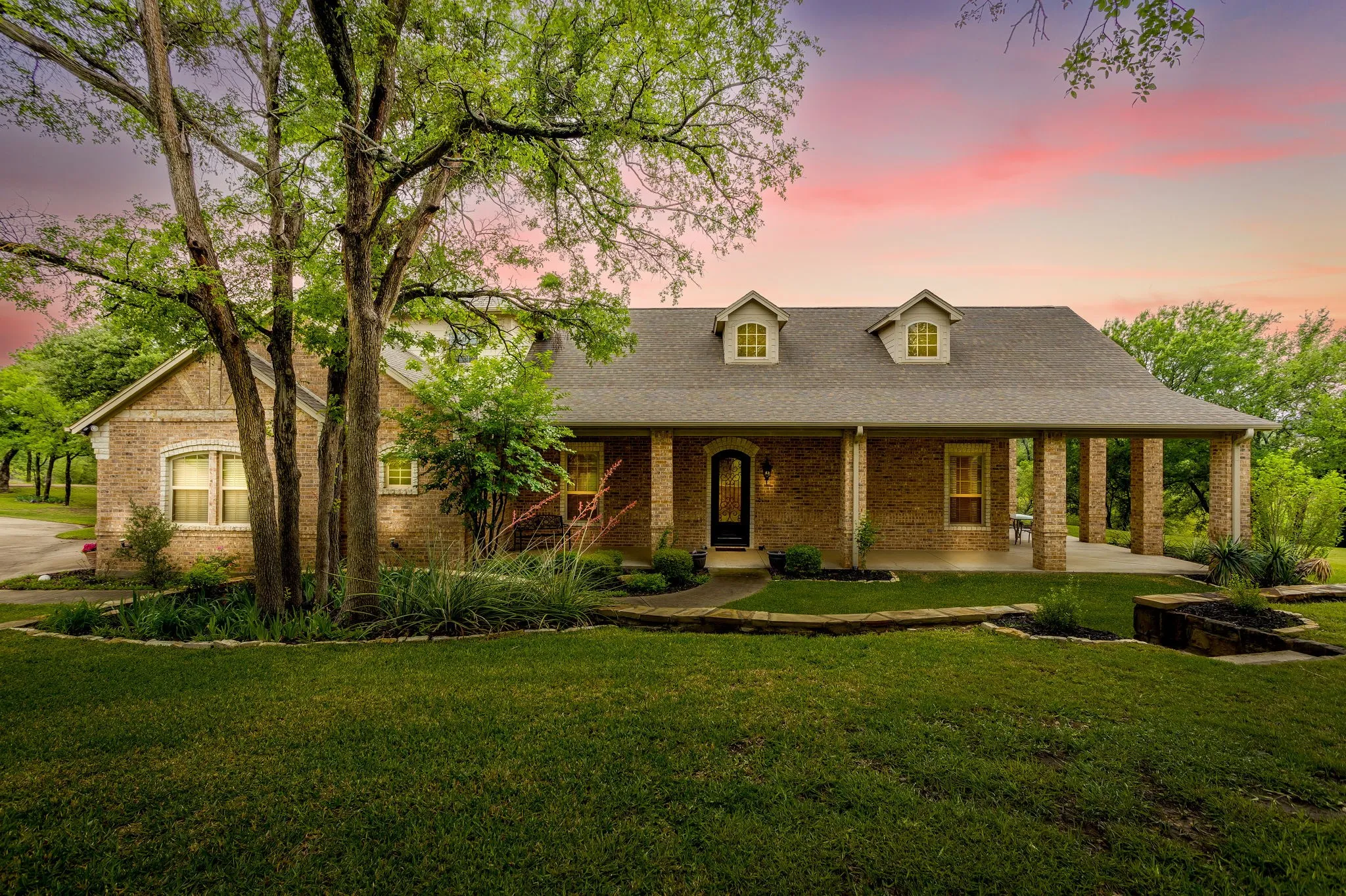 Brick exterior featuring a covered front porch with substantial columns, dark entry door, and dormer windows