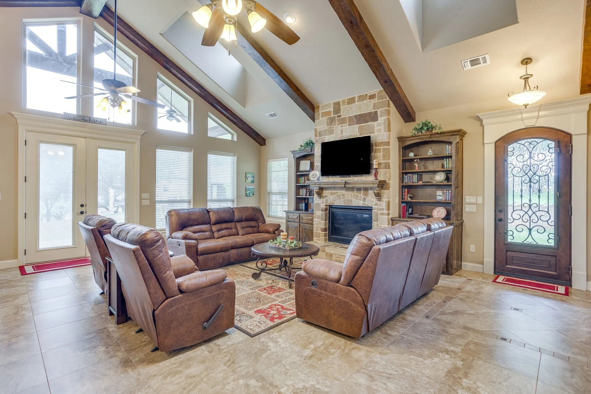 Spacious living area featuring a stone-clad fireplace, vaulted ceiling with exposed wood beams, and tile flooring