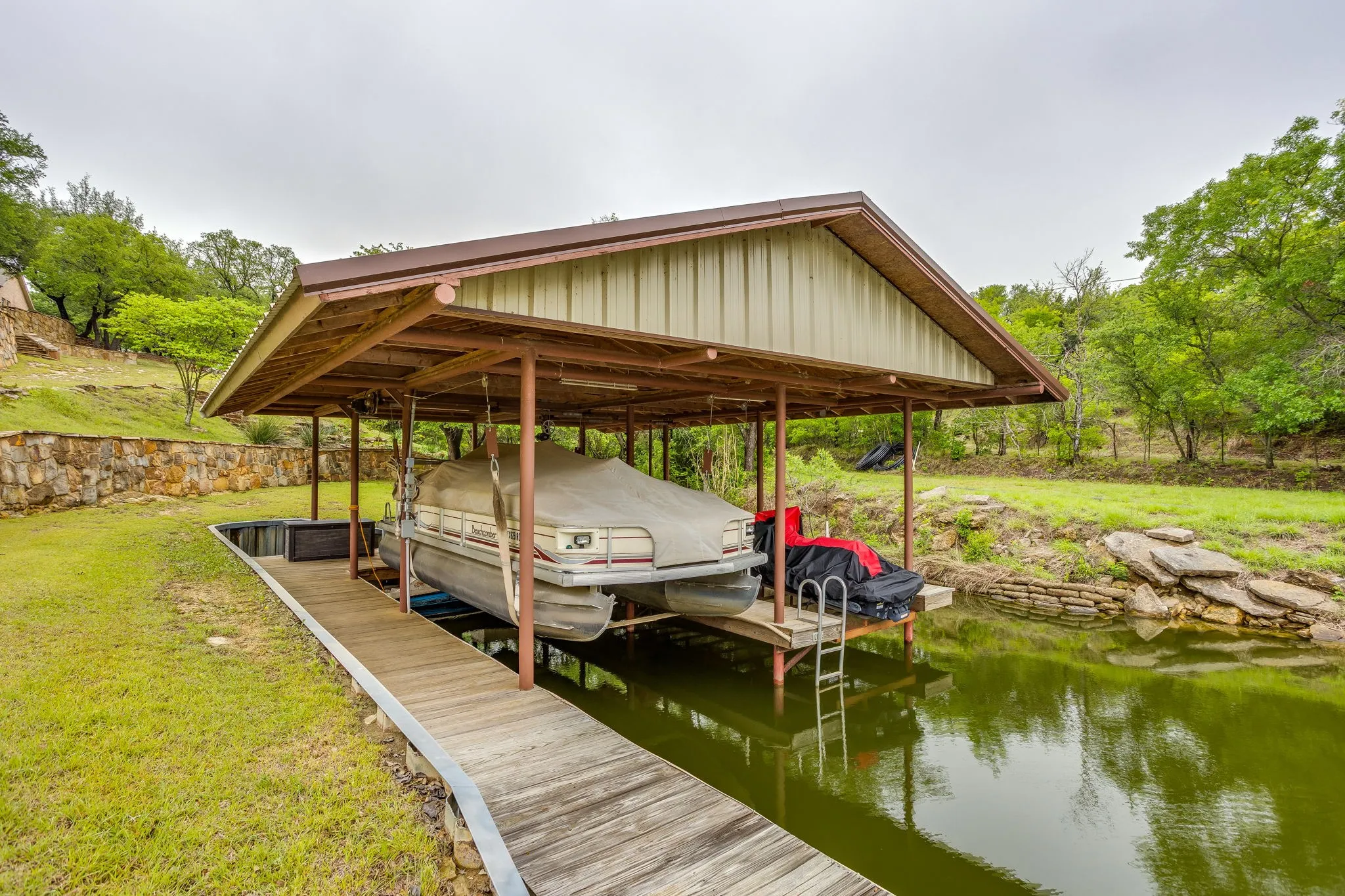 Covered boat dock featuring a metal roof, wood-finish decking, and a built-in ladder for water access