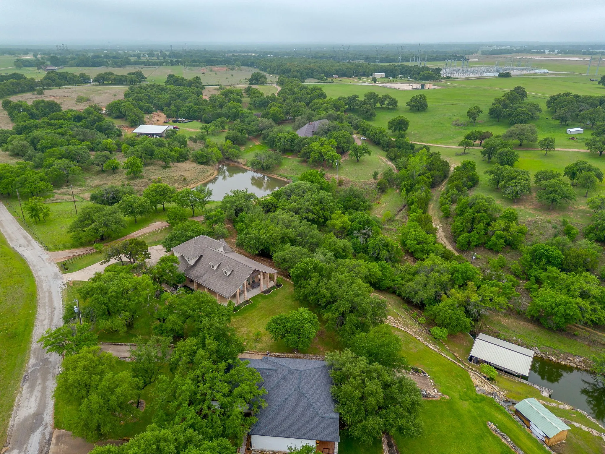 Sprawling property featuring a prominent main residence with a covered porch, multiple water features including a pond and a creek, significant tree coverage, and expansive green spaces