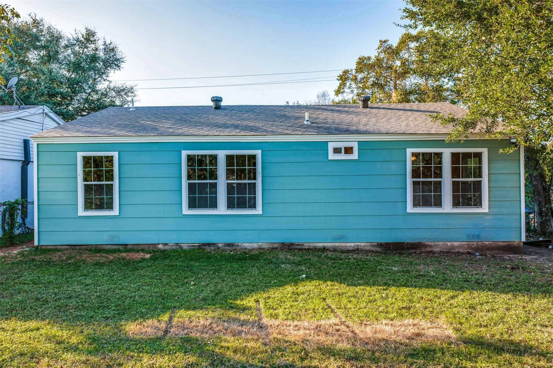 Back of house with a shingled roof and a lawn