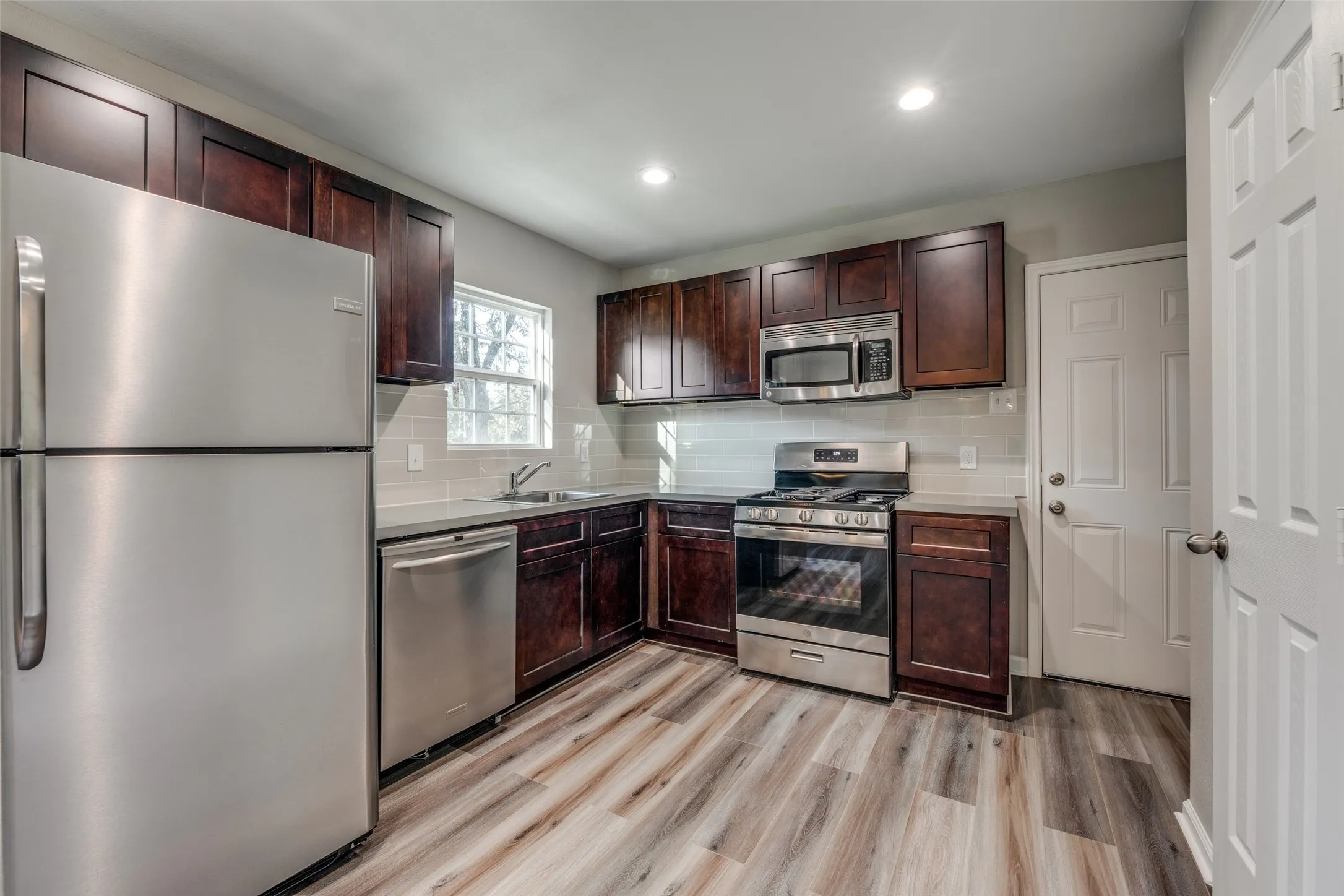 Kitchen with stainless steel appliances, tasteful backsplash, recessed lighting, light wood finished floors, and dark brown cabinets