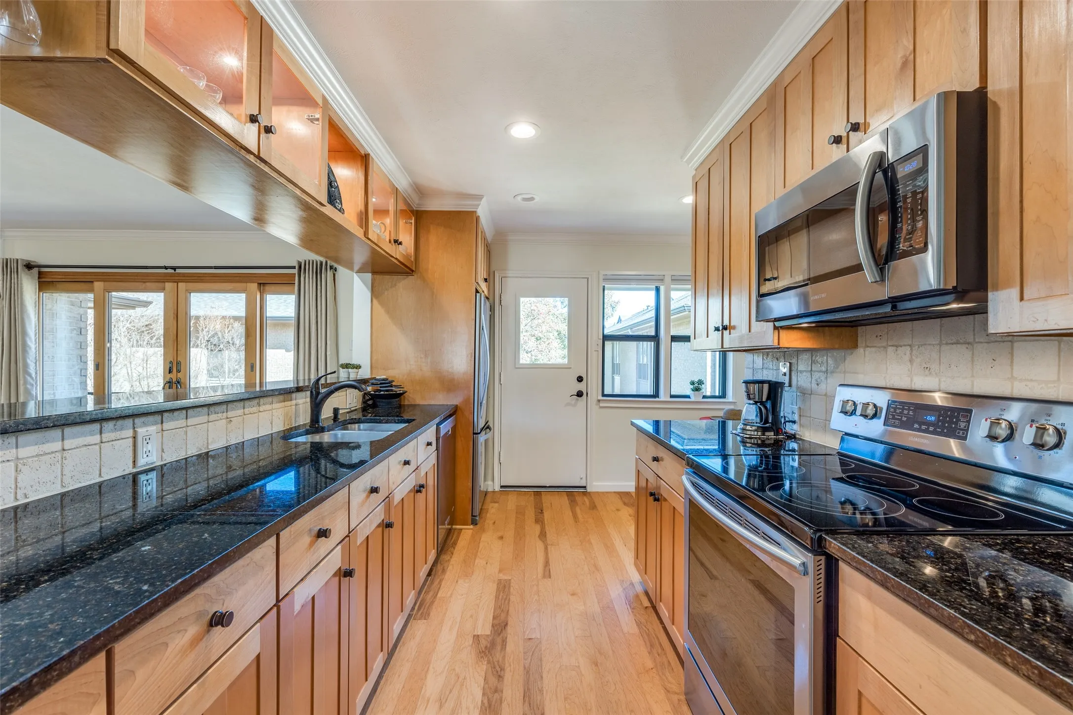 Galley kitchen featuring wood-finish cabinetry, dark granite countertops, and stainless steel appliances