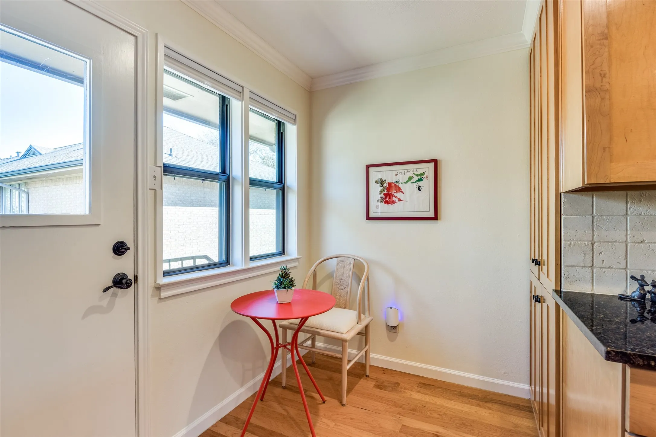 Kitchen nook featuring wood-finish flooring, a white paneled door with a glass insert, multiple windows, a tile backsplash, and dark stone countertops