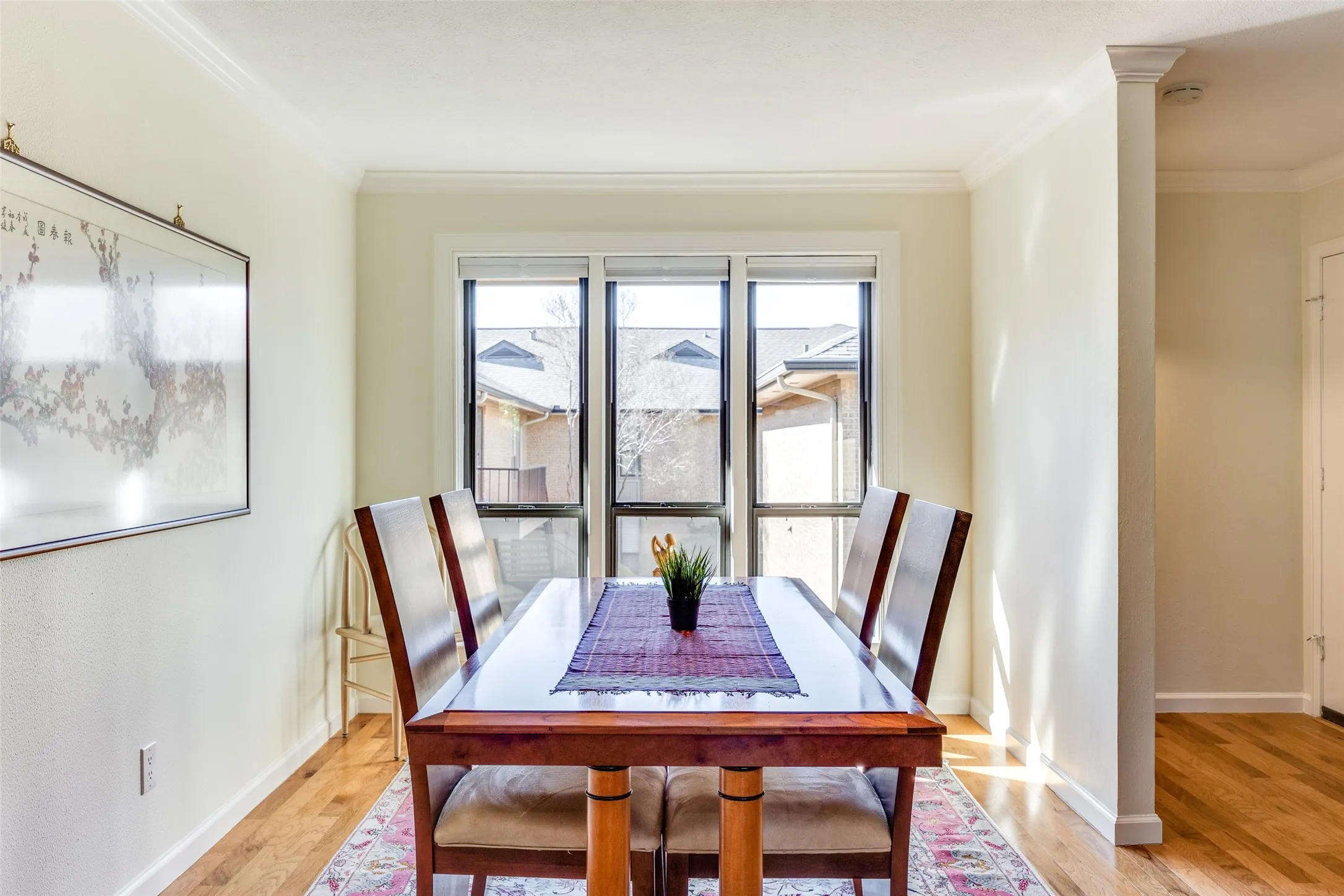 Dining area featuring wood-finish flooring, crown molding, and a window framing exterior rooftops