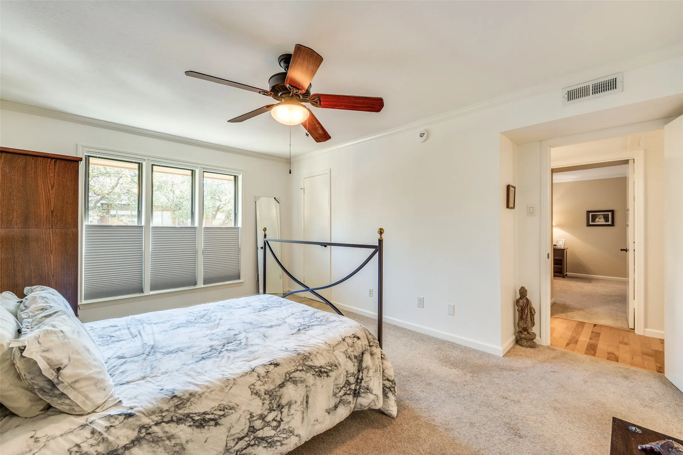 Bedroom featuring a three-pane window with cellular shades, a ceiling fan with light fixture, white walls, and carpet flooring