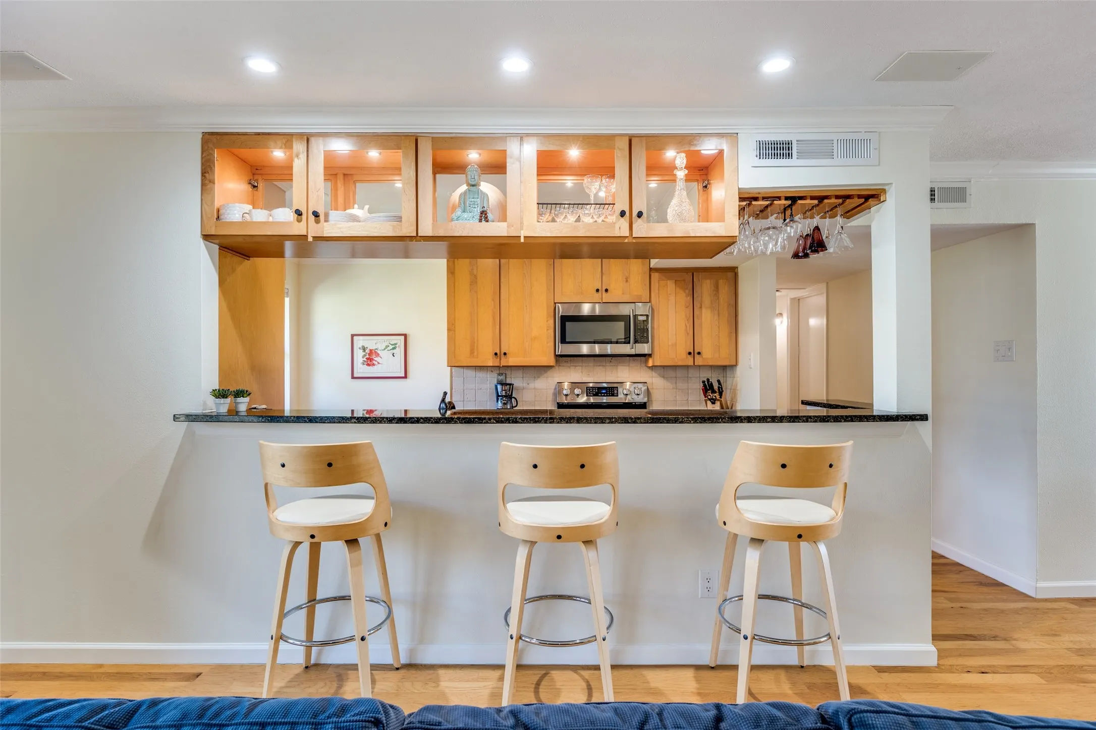 Functional bar area featuring a dark countertop, upper wood cabinetry with glass fronts, under-cabinet lighting, and integrated wine glass storage