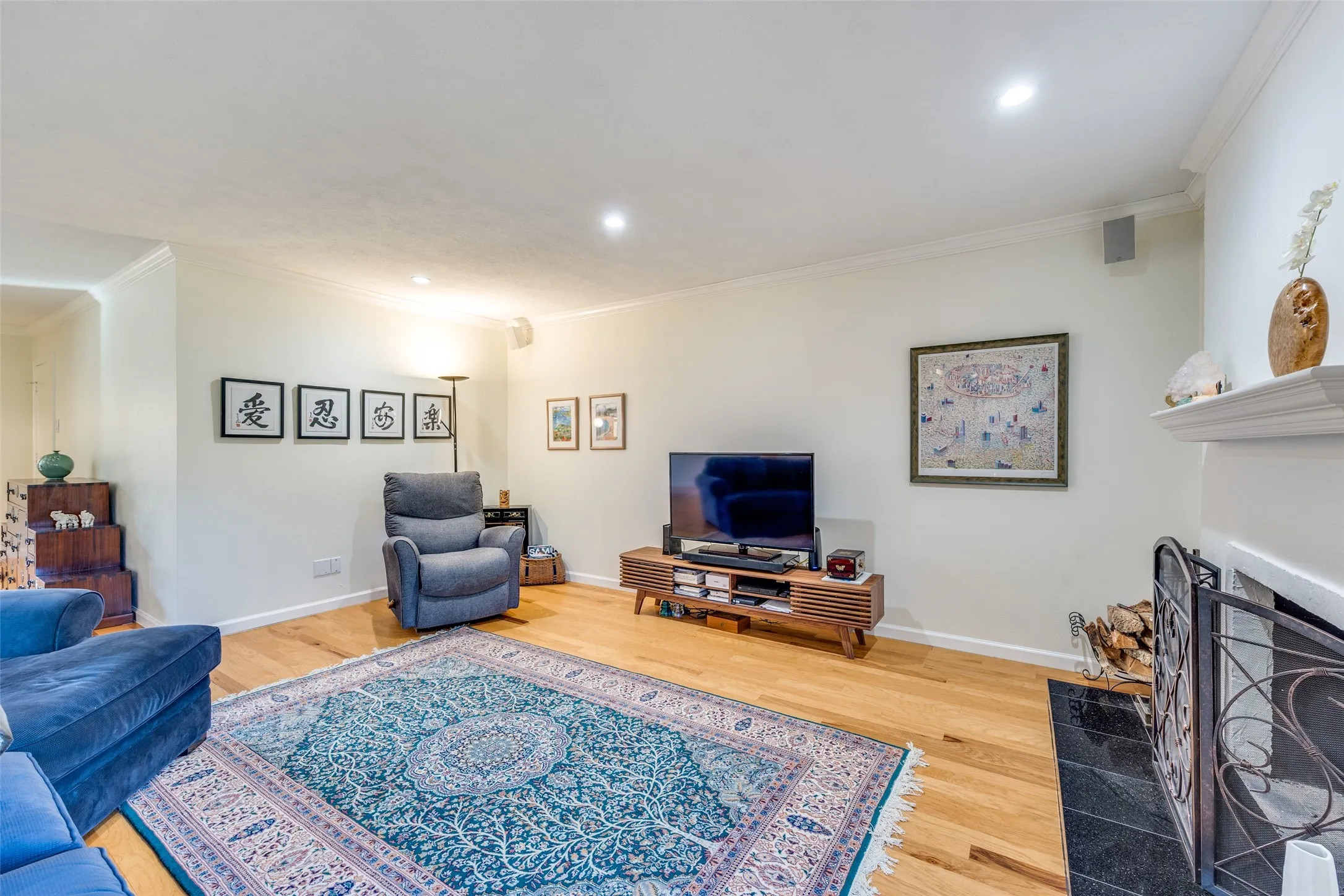 Living area featuring wood-finish flooring, recessed lighting, crown molding, and a fireplace with a black tile hearth and decorative screen