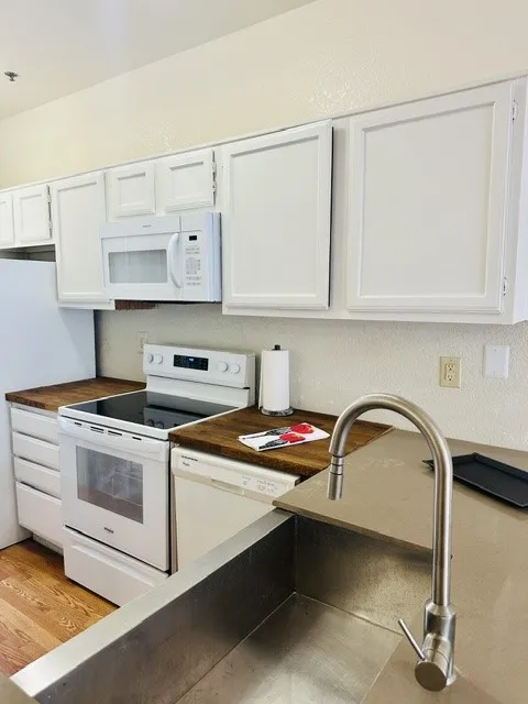 Kitchen featuring white cabinetry, wood-finish countertops, and a stainless steel sink with a gooseneck faucet